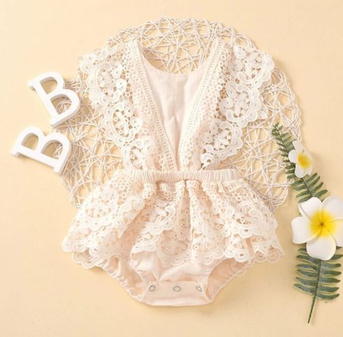 Detailed white lace baby romper with bow detail and floral decorative elements.