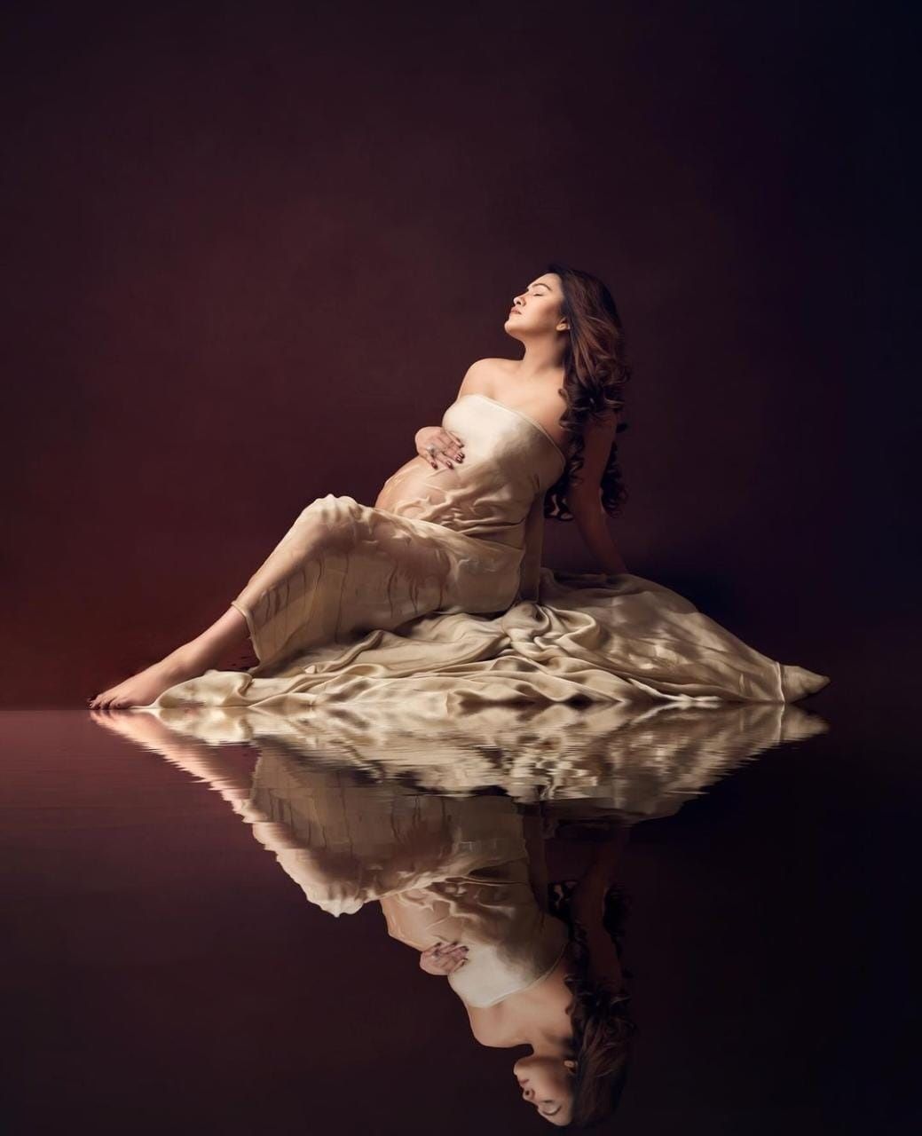 Dramatic maternity photos with reflection effect against dark background.
