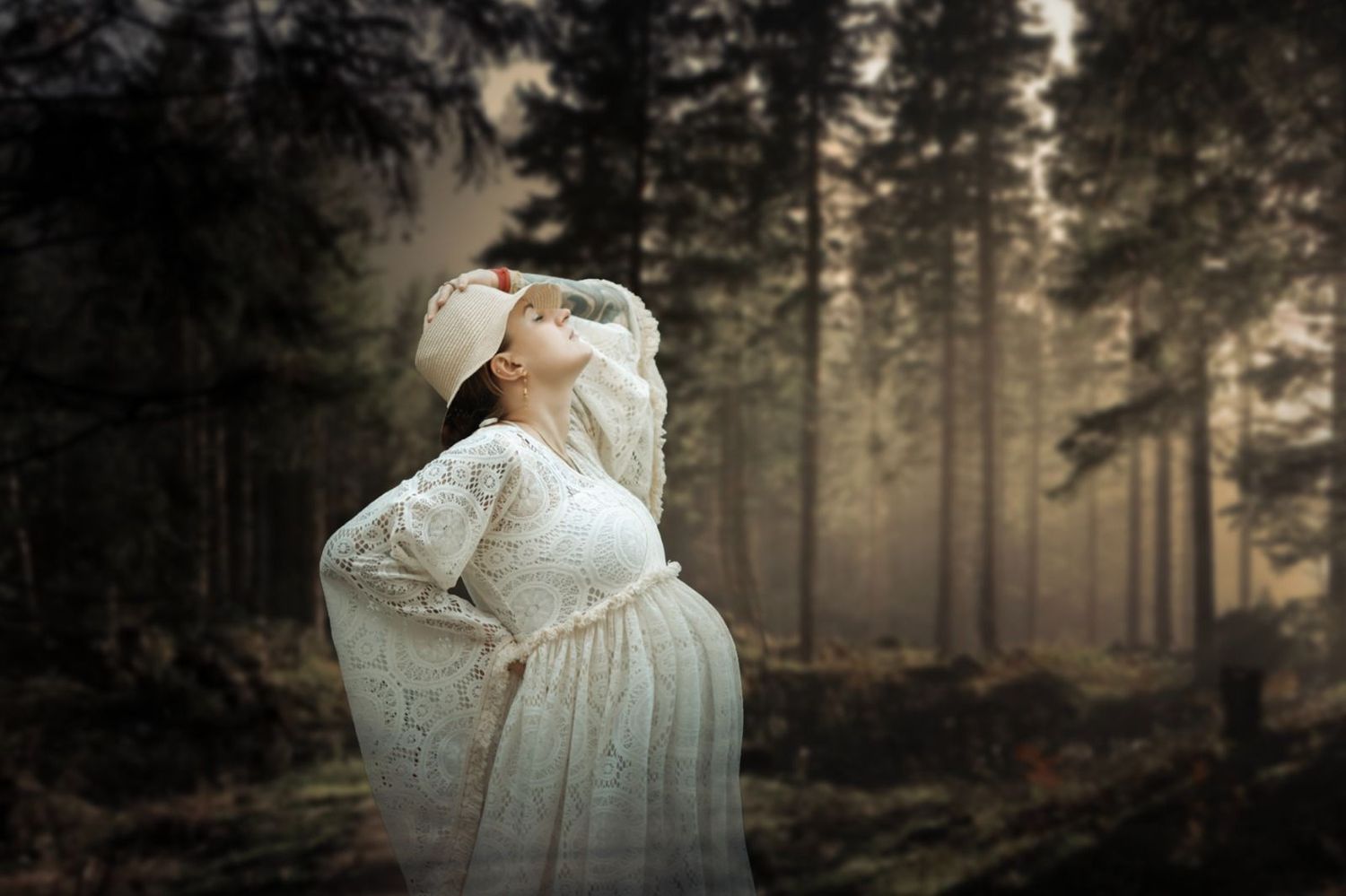 Romantic maternity silhouettes captured in misty forest setting with dramatic backlighting.
