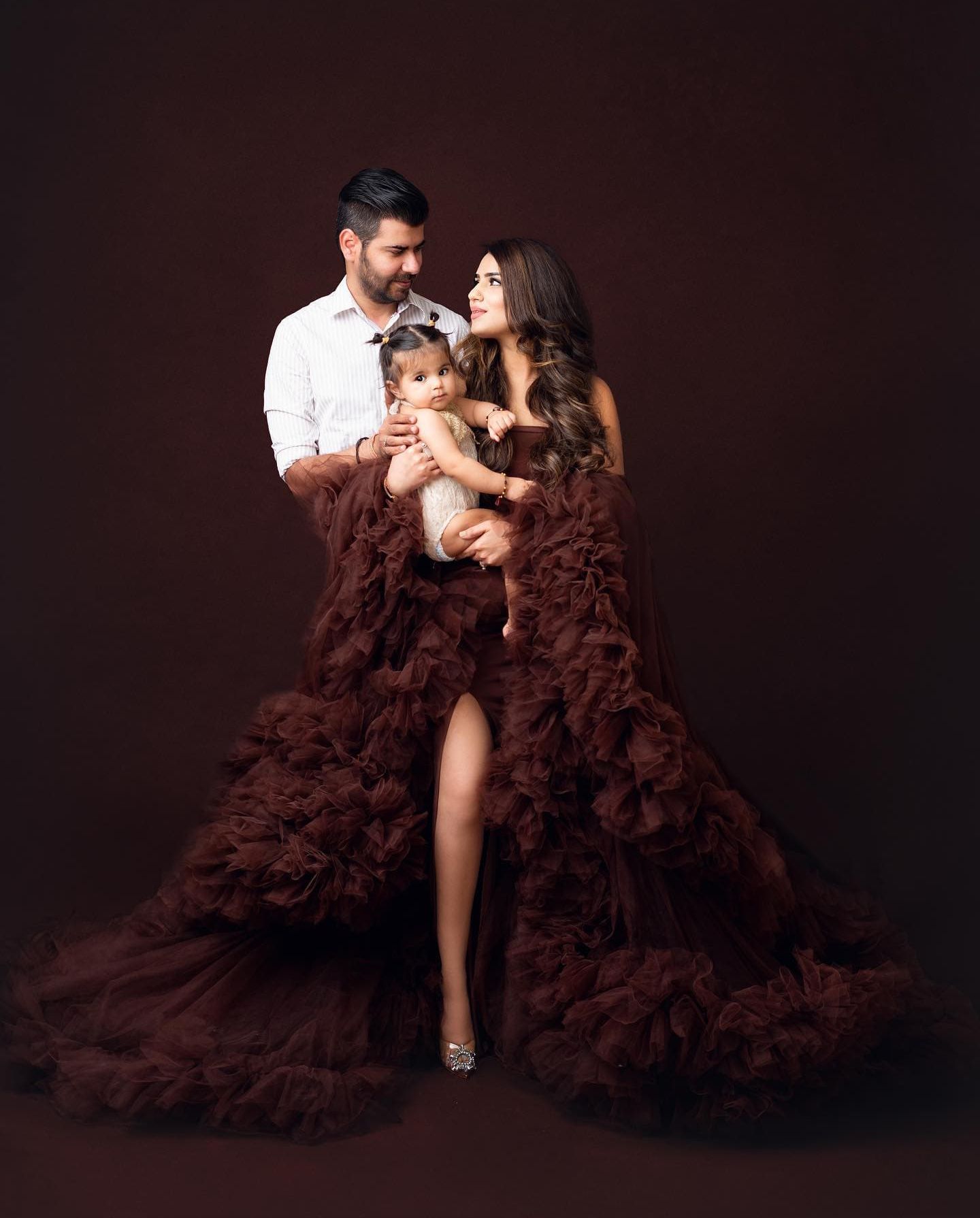 Family maternity portrait in coordinating brown and white outfits against dark studio background.