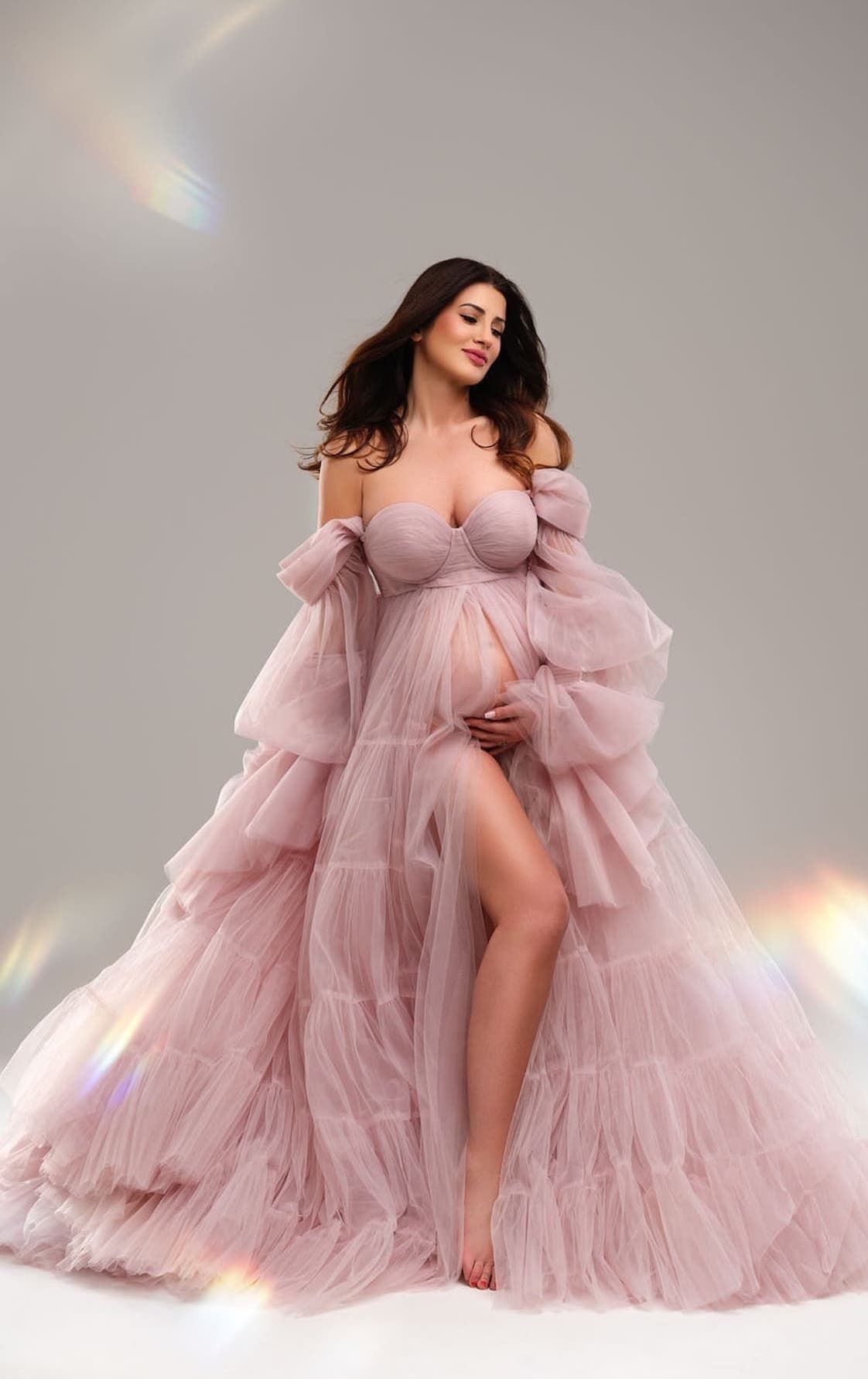 Flowing pink tulle maternity gown with dramatic ruffles against light backdrop.