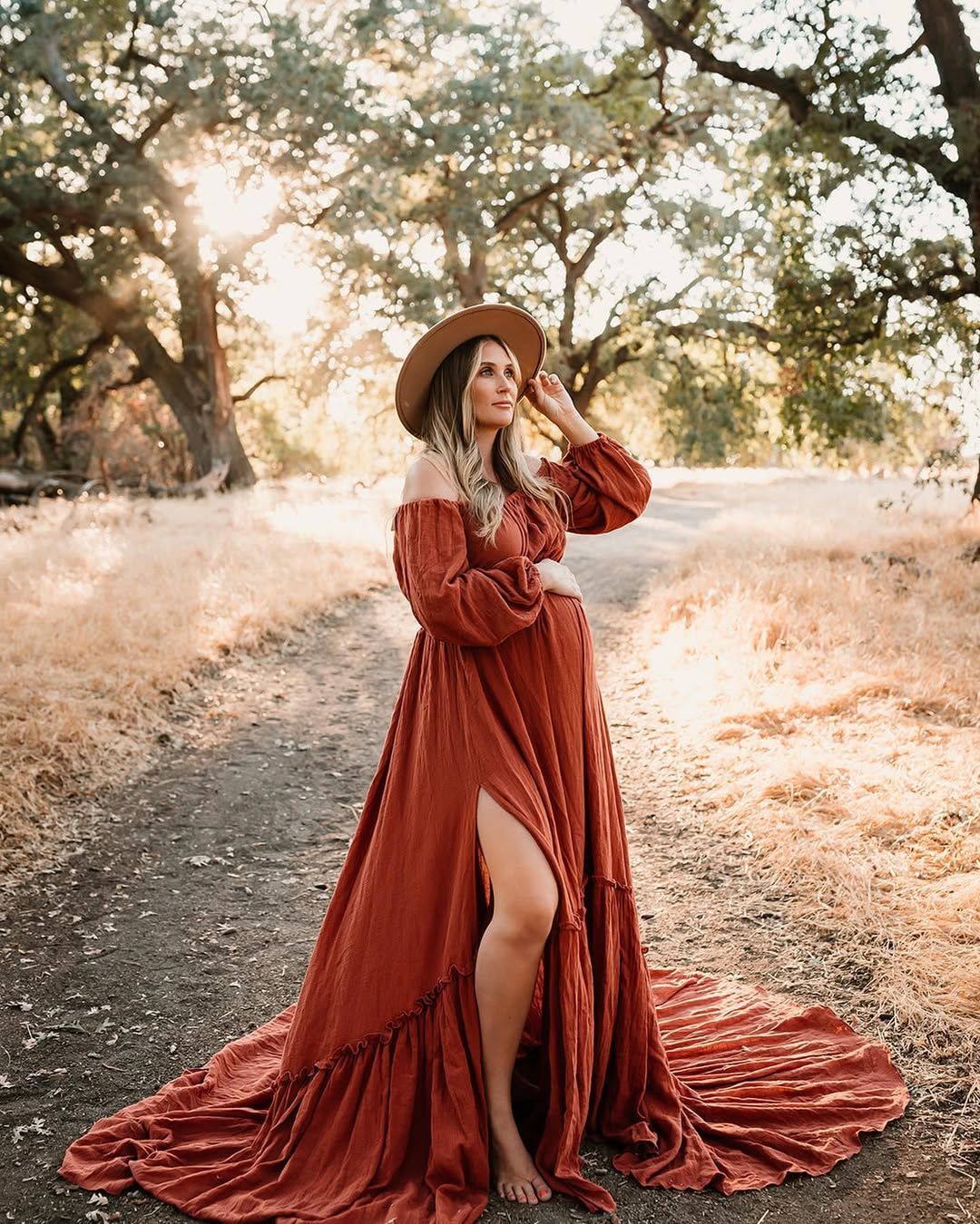 Boho style maternity photo with red maxi dress and hat in golden sunset light.