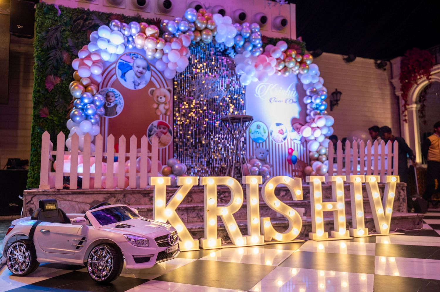 Illuminated KRISHIV letter marquee sign with balloon arch and toy car at a colorful birthday party celebration.