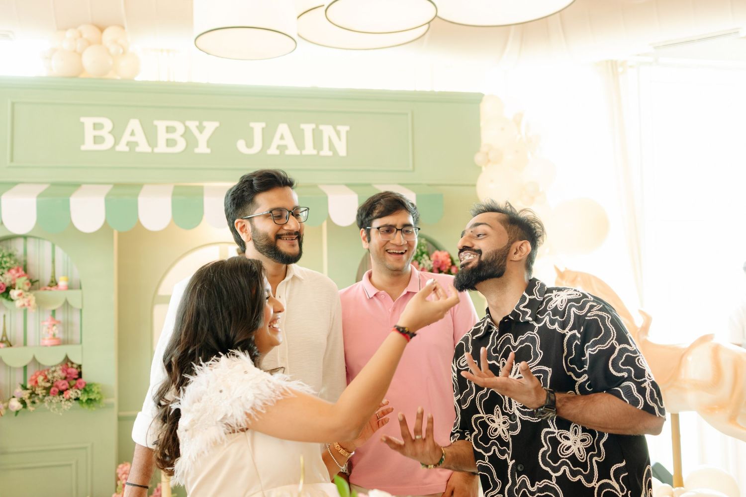 Four friends laugh and celebrate at a Baby Jain baby shower party with floral decorations.