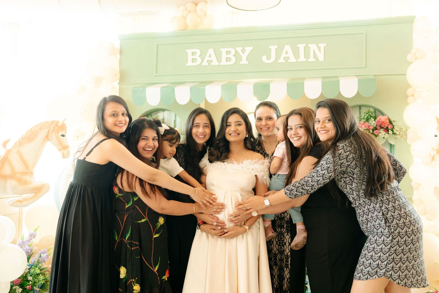 Group of women posing together at a Baby Jain baby shower, with the pregnant guest of honor in the center.