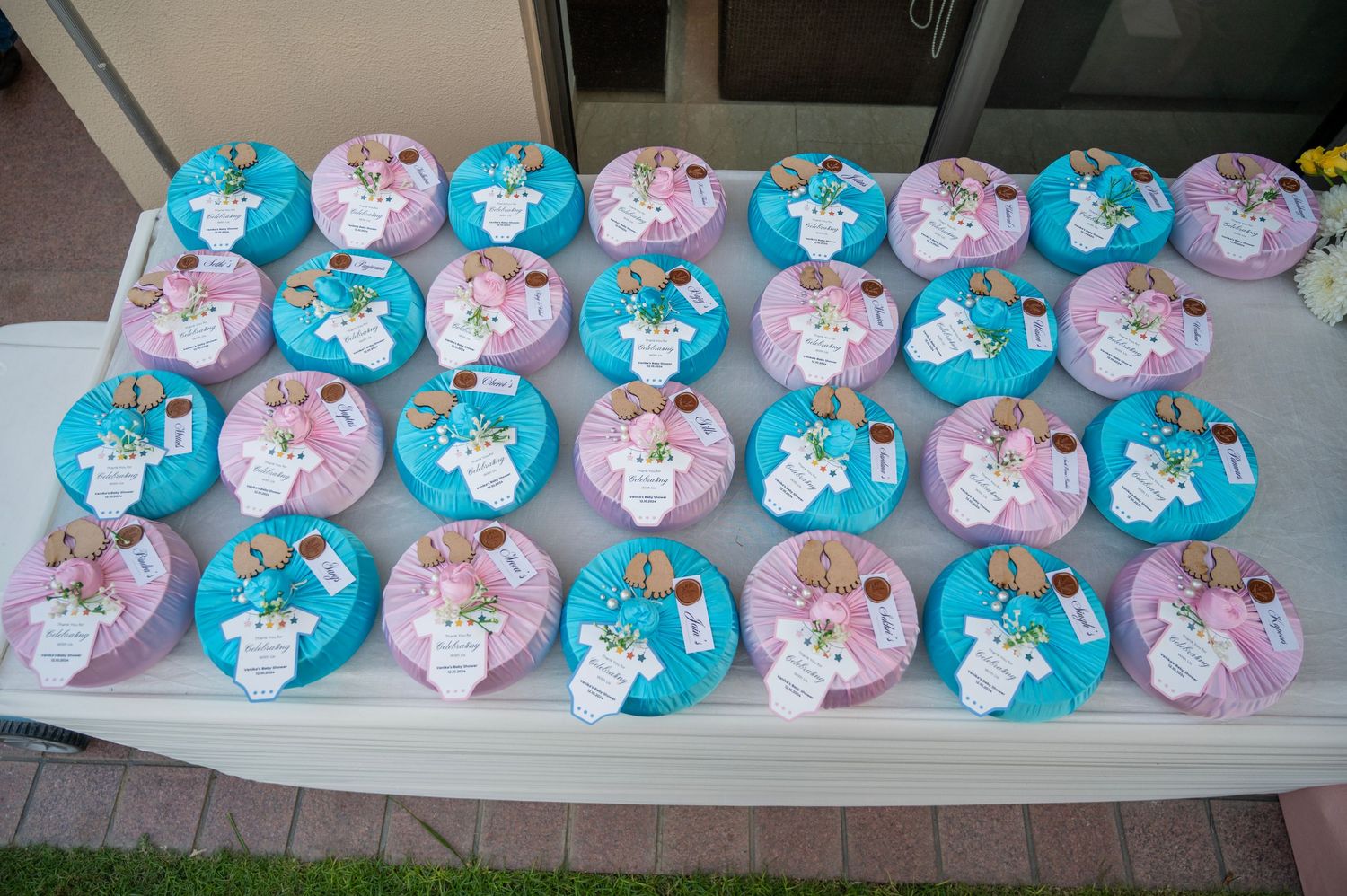 Colorful pink and blue decorated mini cakes with floral toppers displayed on a white table for a baby shower.