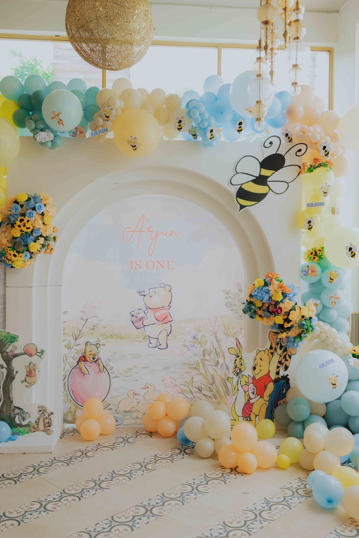 Winnie the Pooh first birthday party backdrop with balloon garland, bee decorations, and floral arrangements.