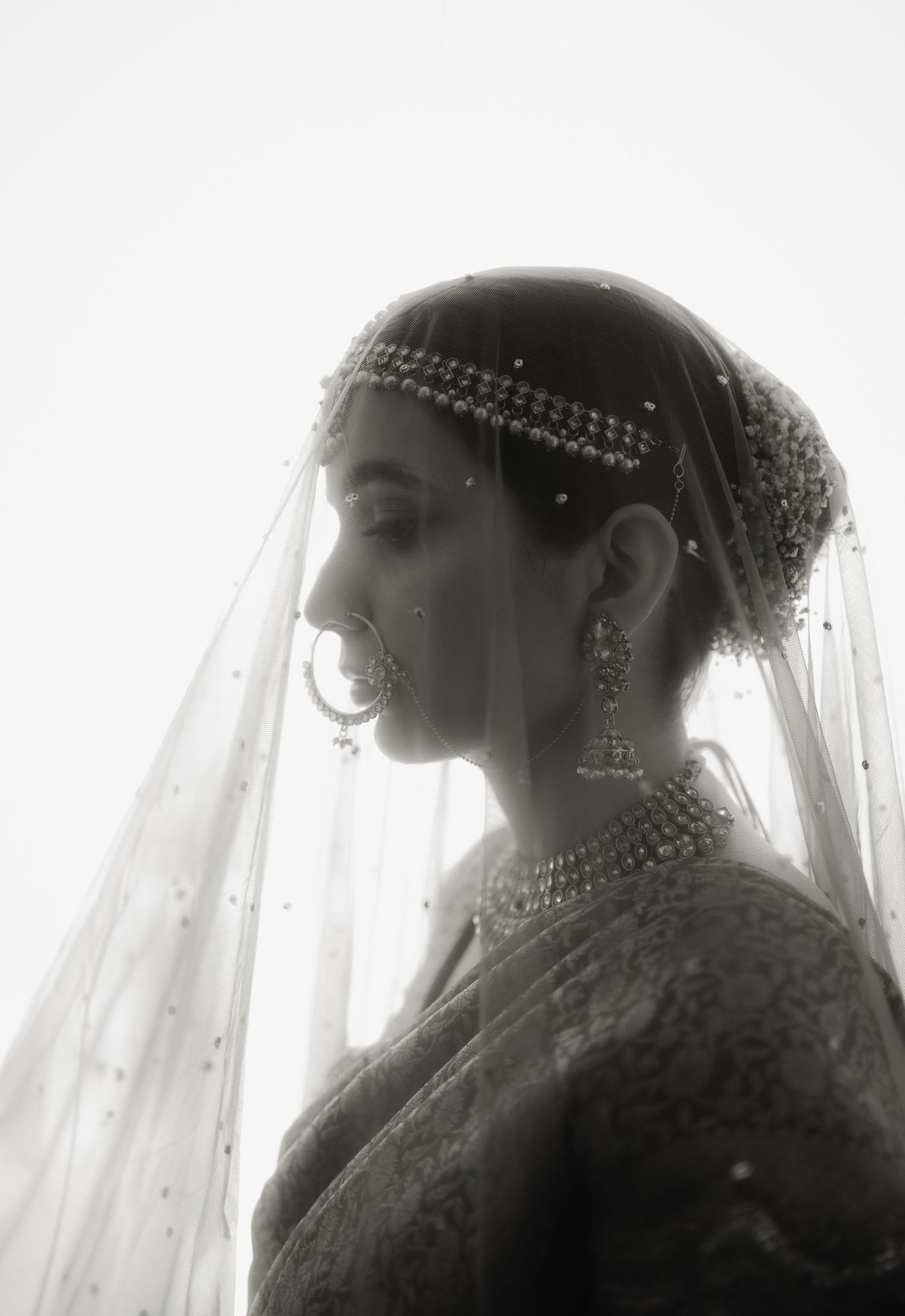 Black and white portrait of a South Asian bride wearing traditional jewelry, maang tikka, nath, and embroidered dupatta.