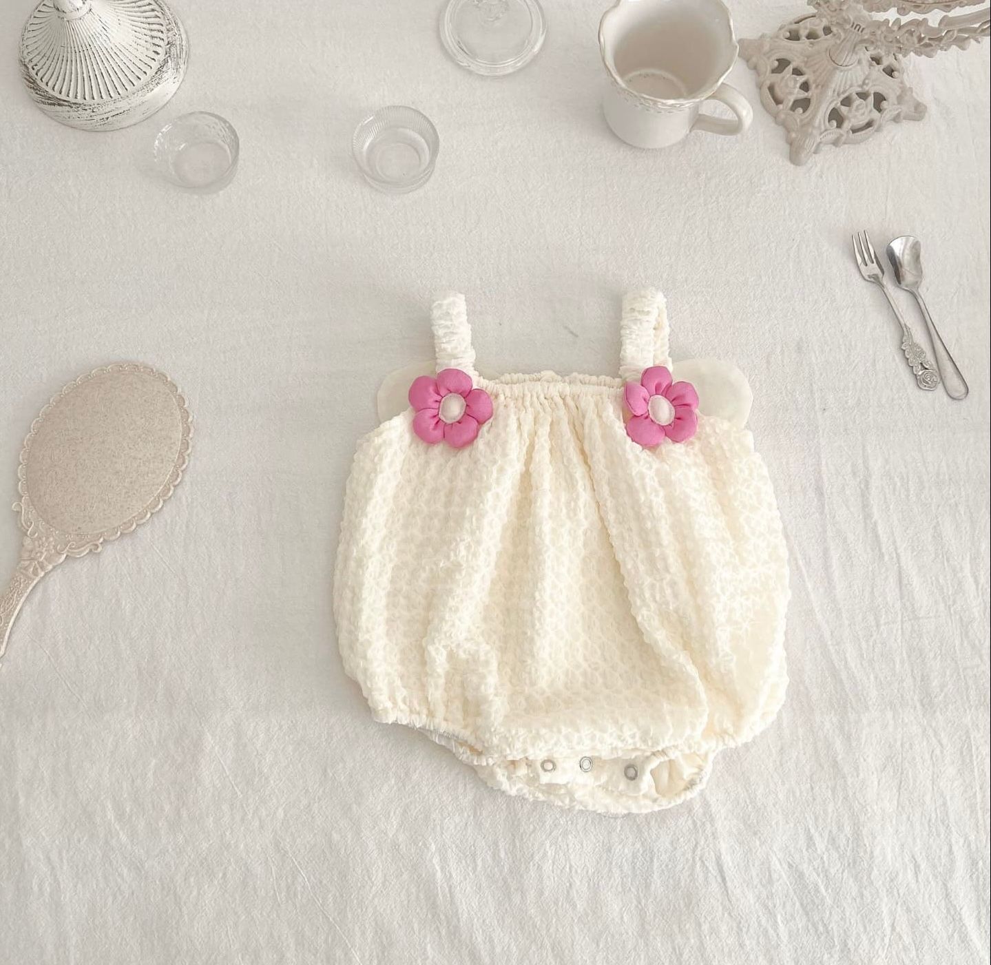 Vintage inspired cream colored baby bloomers with pink flower accents displayed on white surface.