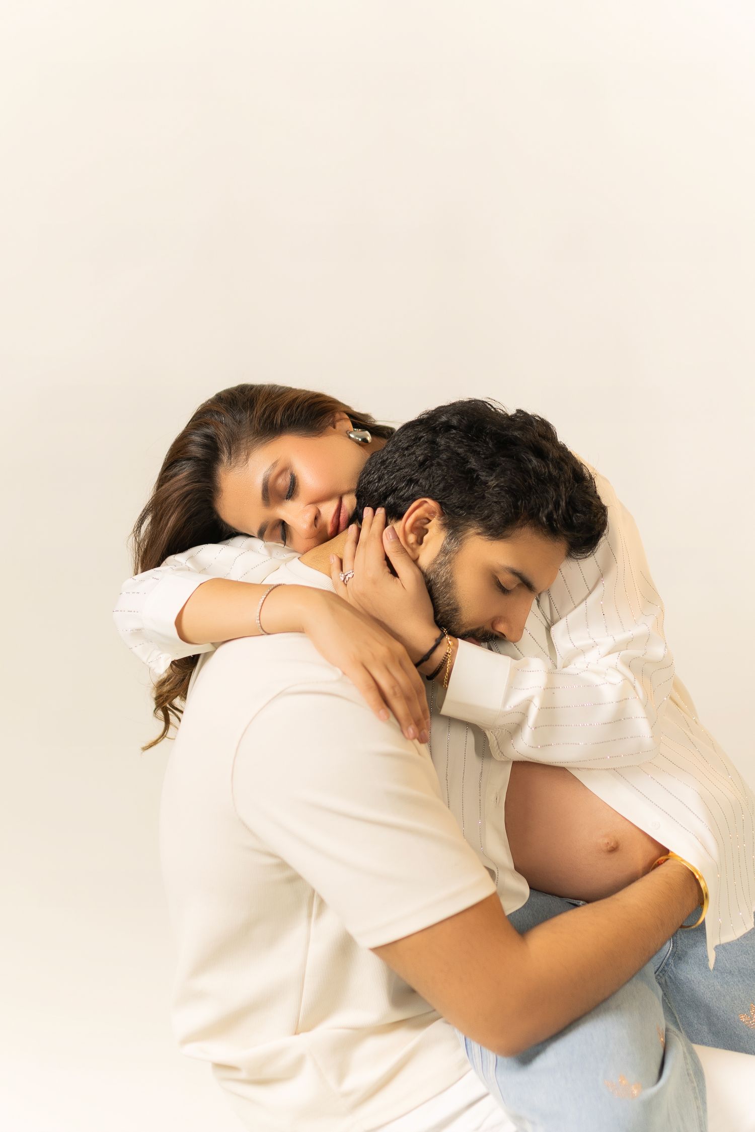 Intimate moment between couple embracing with exposed pregnant belly against light background.
