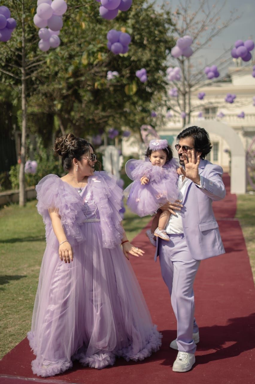 Family in matching lavender outfits celebrating at an outdoor event decorated with purple balloons.
