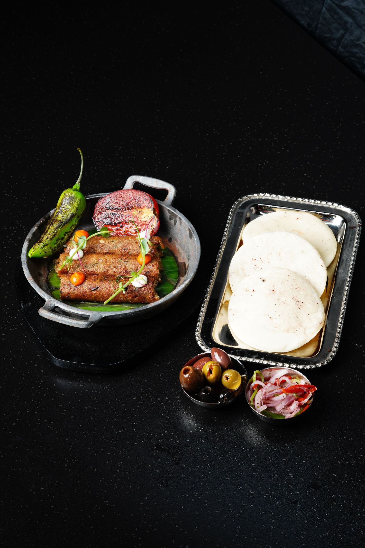 Various small plates of appetizers and bread arranged on black surface with dramatic dark background.