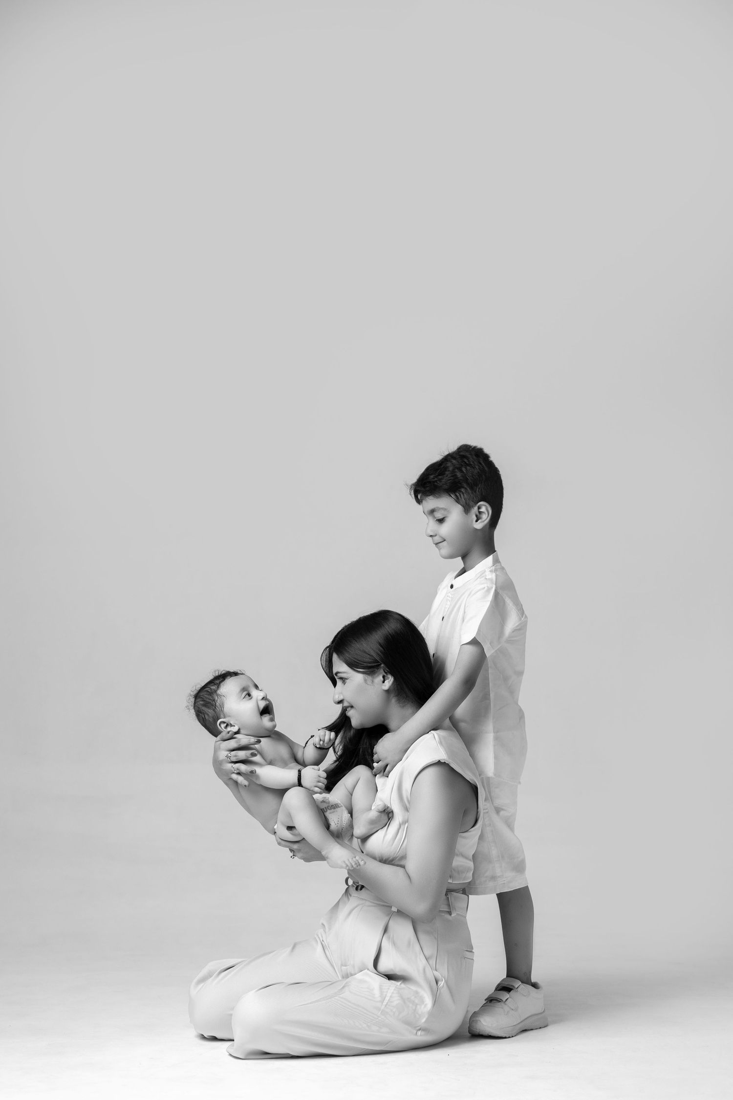 Black and white photo of a mother kneeling while holding a newborn baby, with her young son standing beside her.