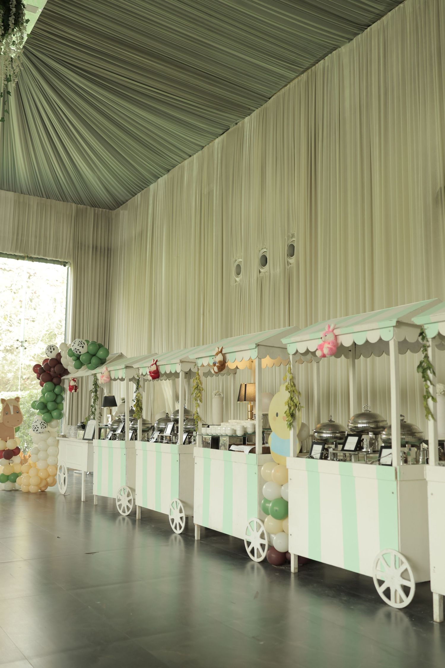 Elegant event venue with mint green striped food carts, balloon decorations, and draped ceiling for a festive celebration.