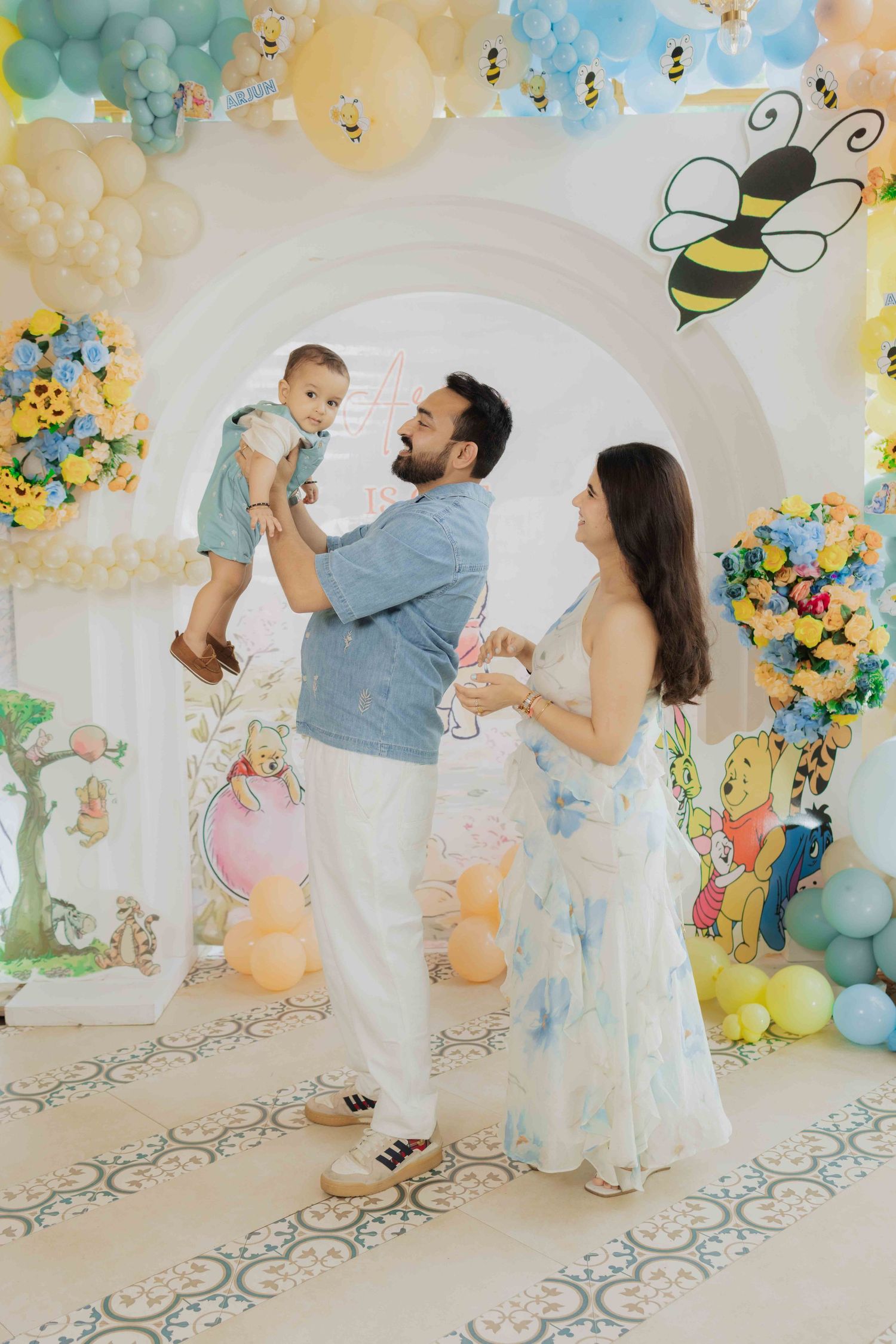 Family celebrating baby's first birthday at a Winnie the Pooh themed party with balloon arch and bee decorations.