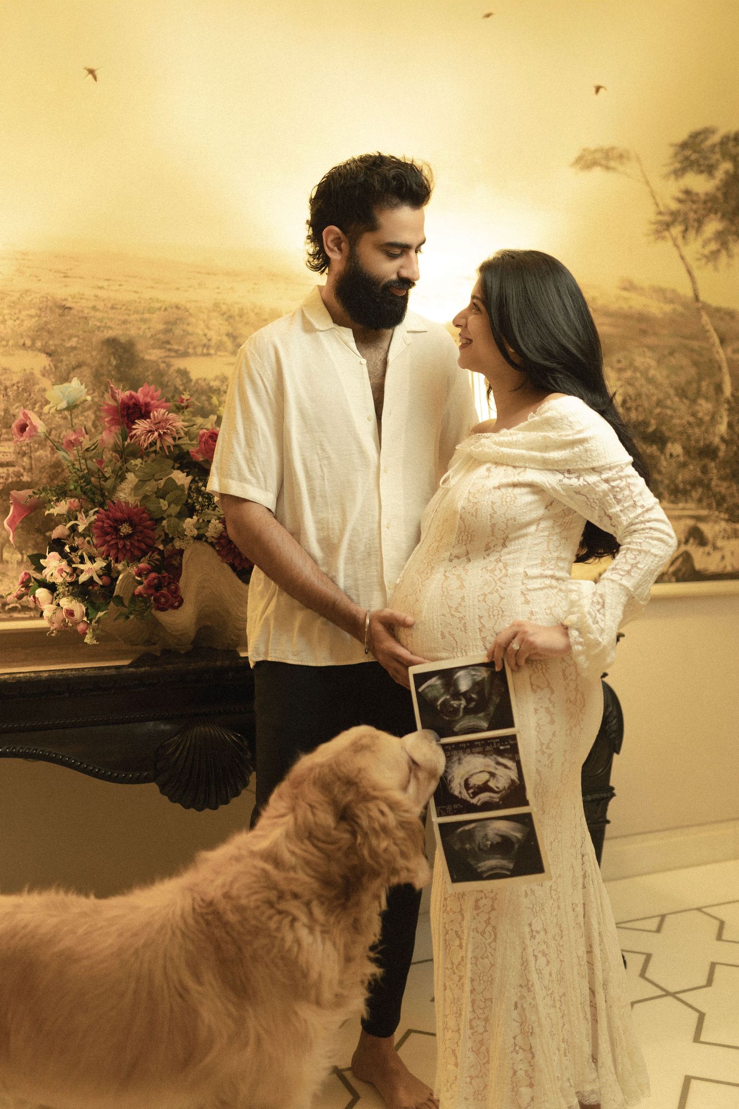A loving couple in white attire share a maternity announcement moment with their golden retriever and ultrasound photo.