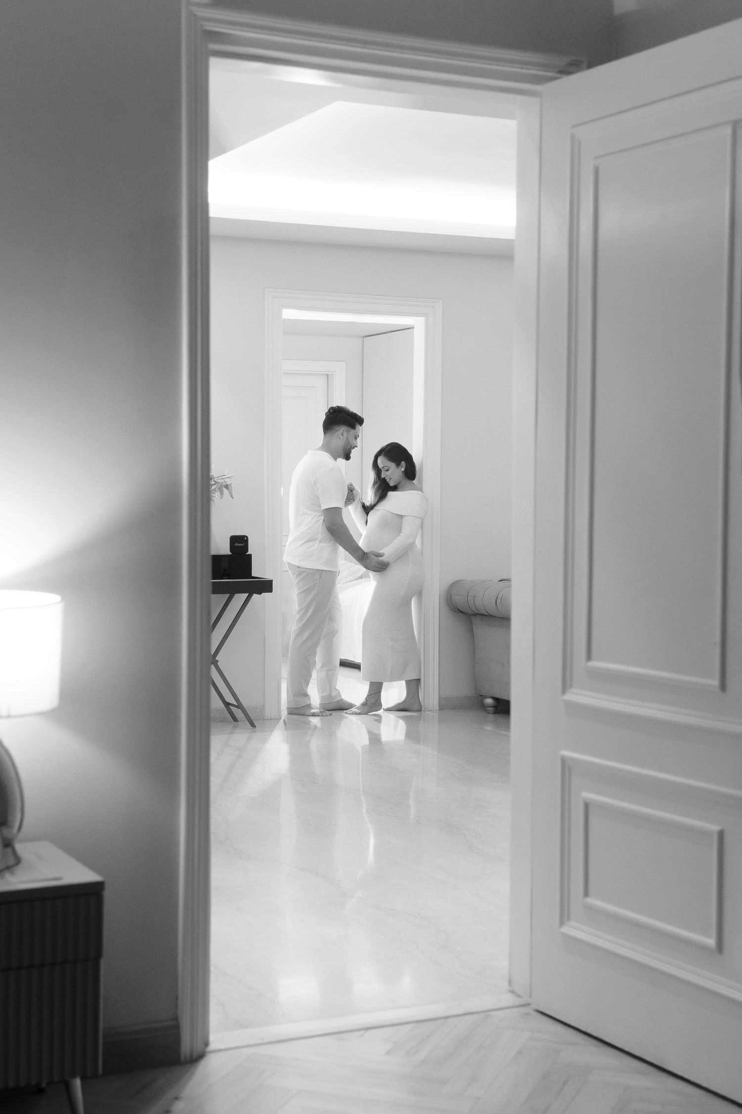 Two figures in white stand in a minimalist white room with doorways creating a stark architectural composition.