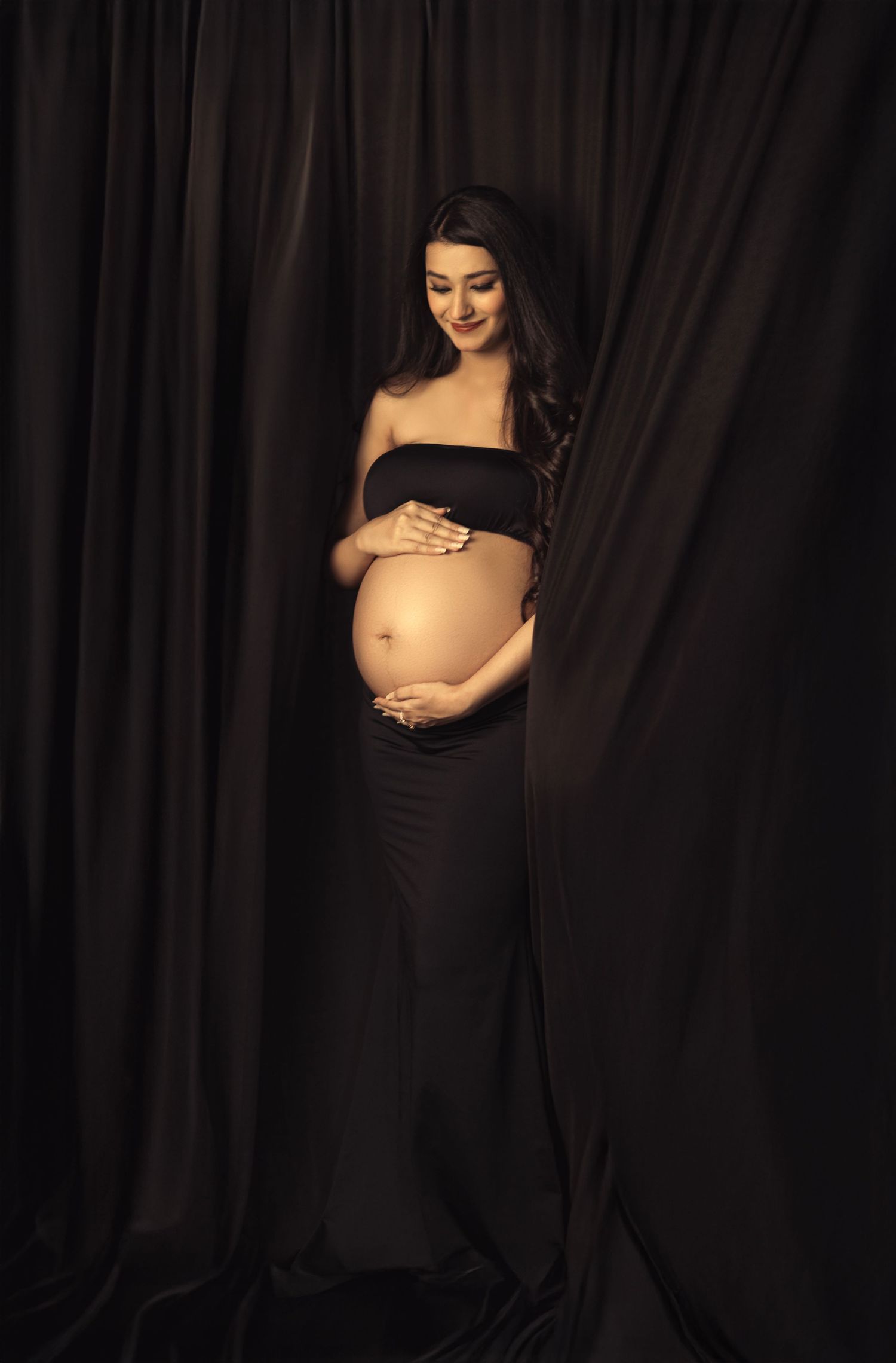 Artistic maternity portraits in dark and moody lighting against black backdrop.