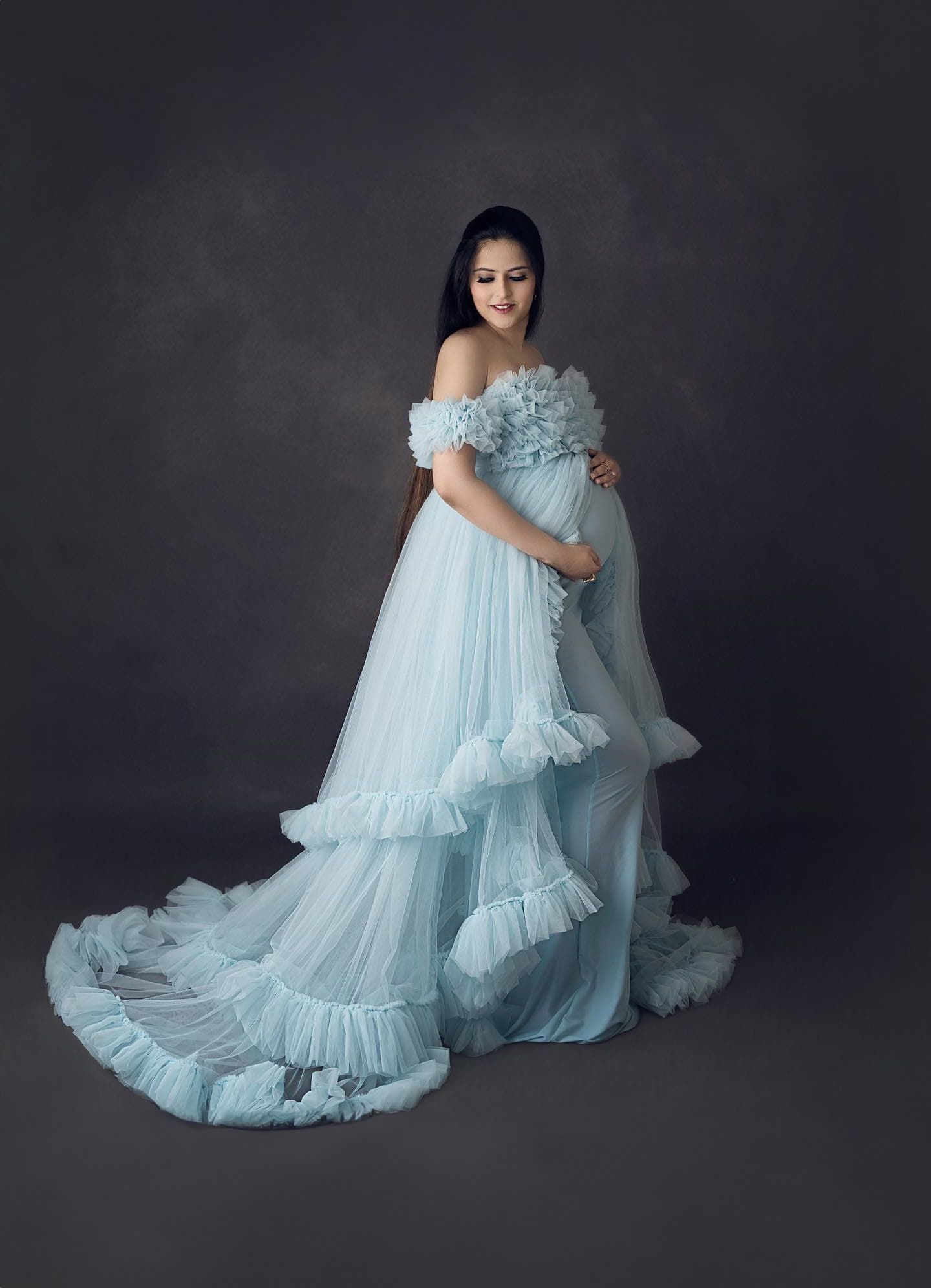 Studio maternity photos showcasing an elegant light blue ruffled gown against a dark backdrop.