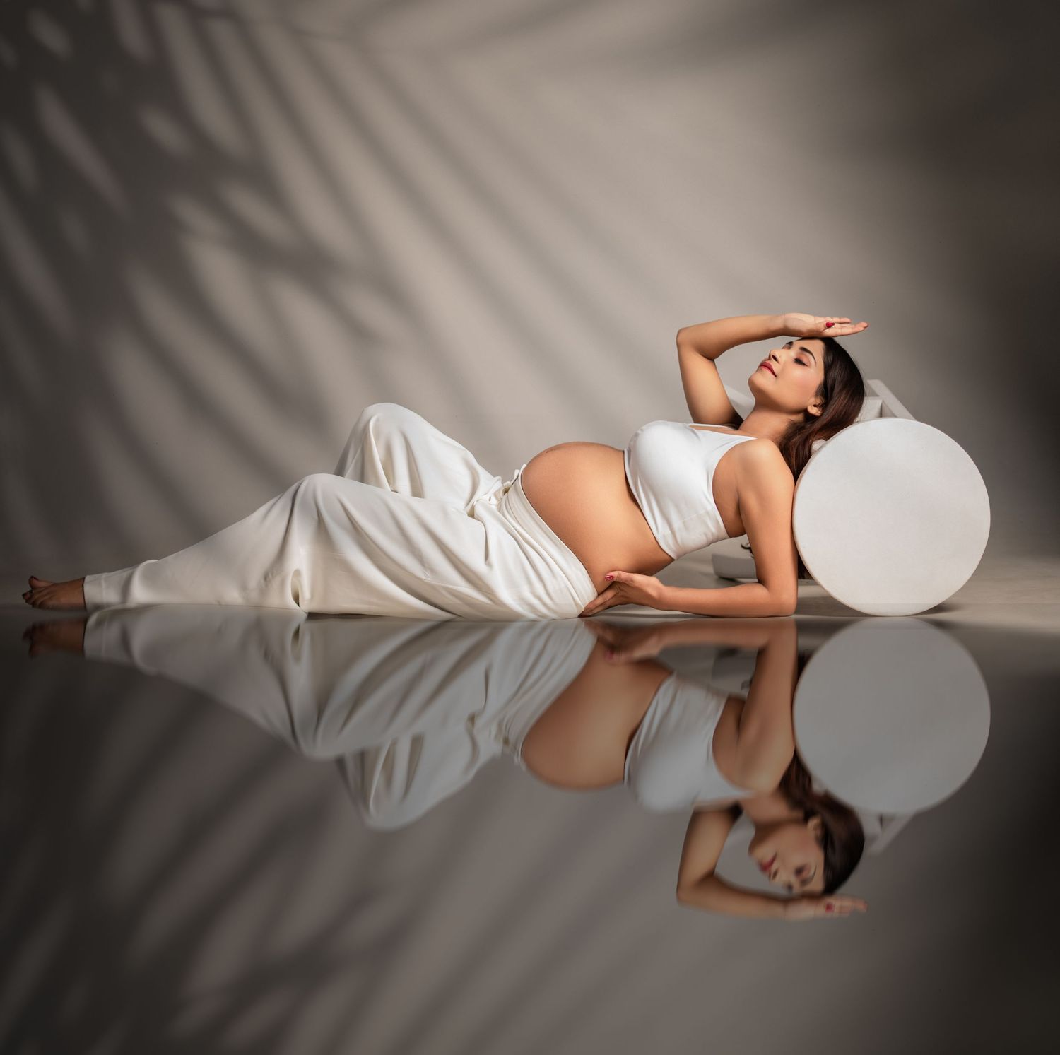 Artistic pregnancy photo with white dress and reflective surface creating mirror effect.