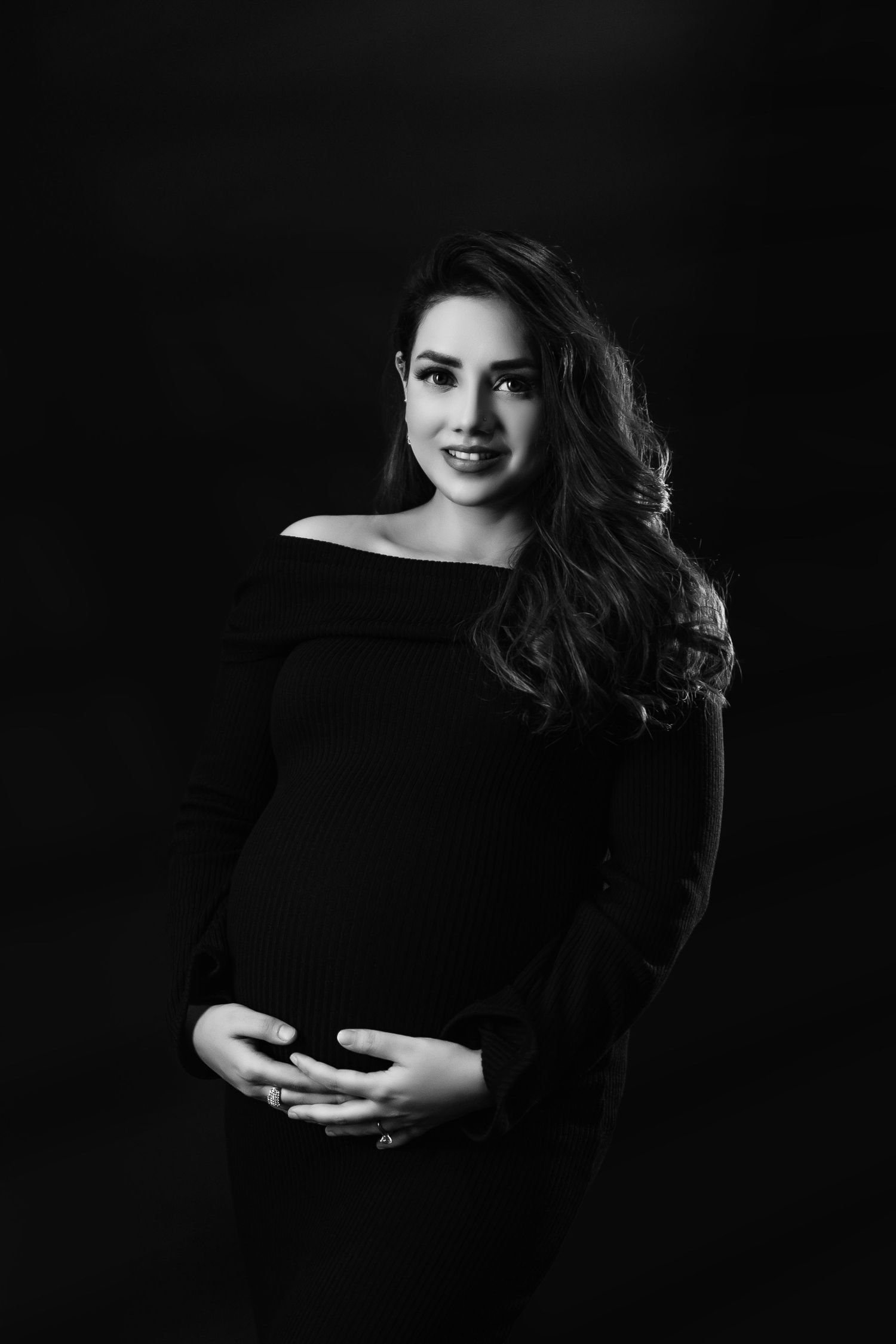 Artistic maternity photography with moody lighting and black background.