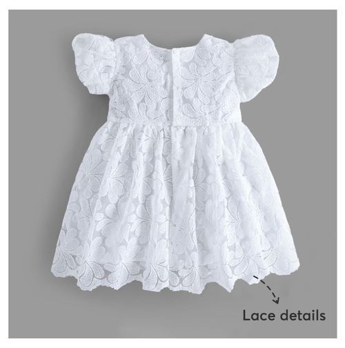 White lace baby dress with puff sleeves and floral embroidery details shown against gray background.