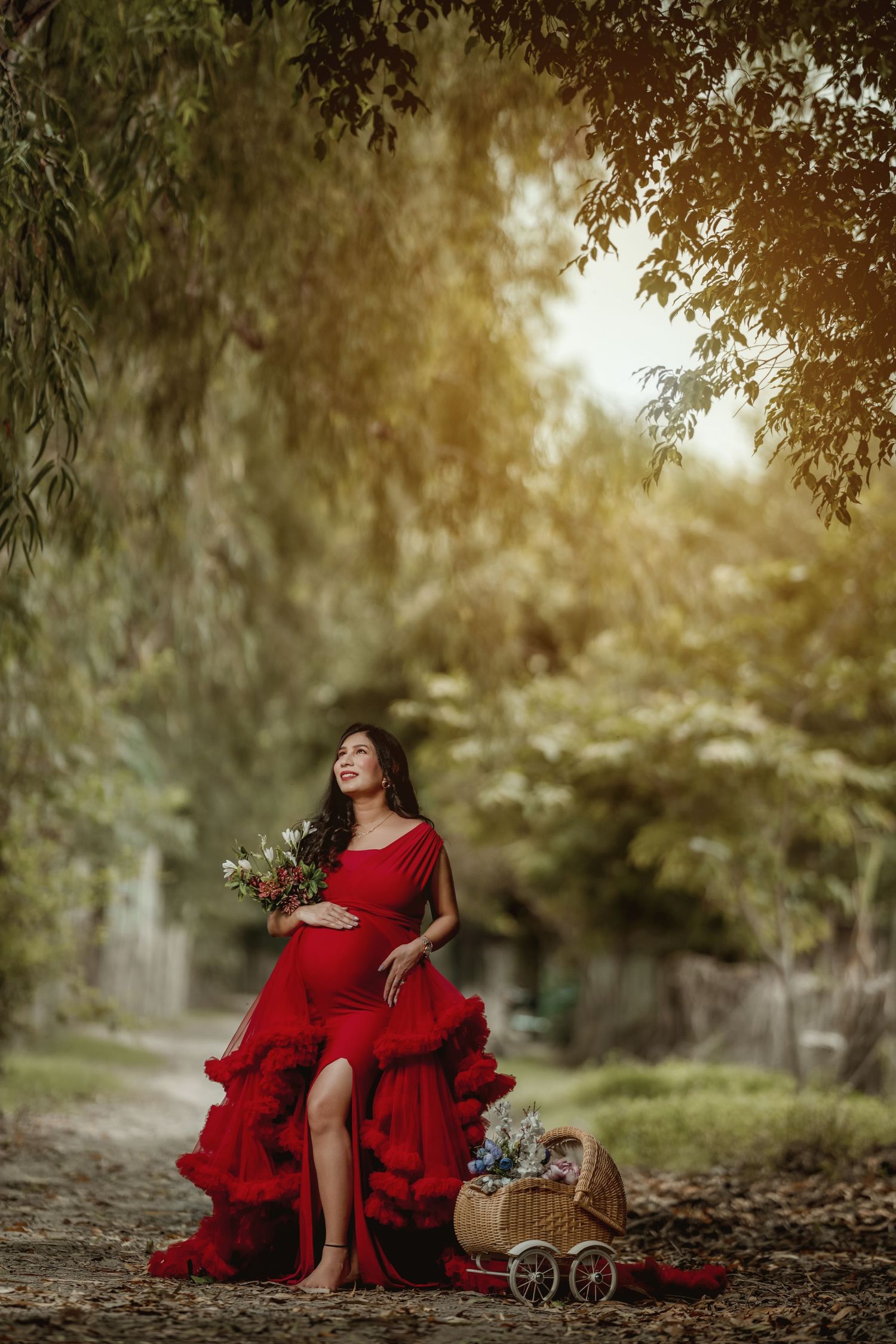 Outdoor maternity photo with red ruffled dress and vintage style baby carriage prop.