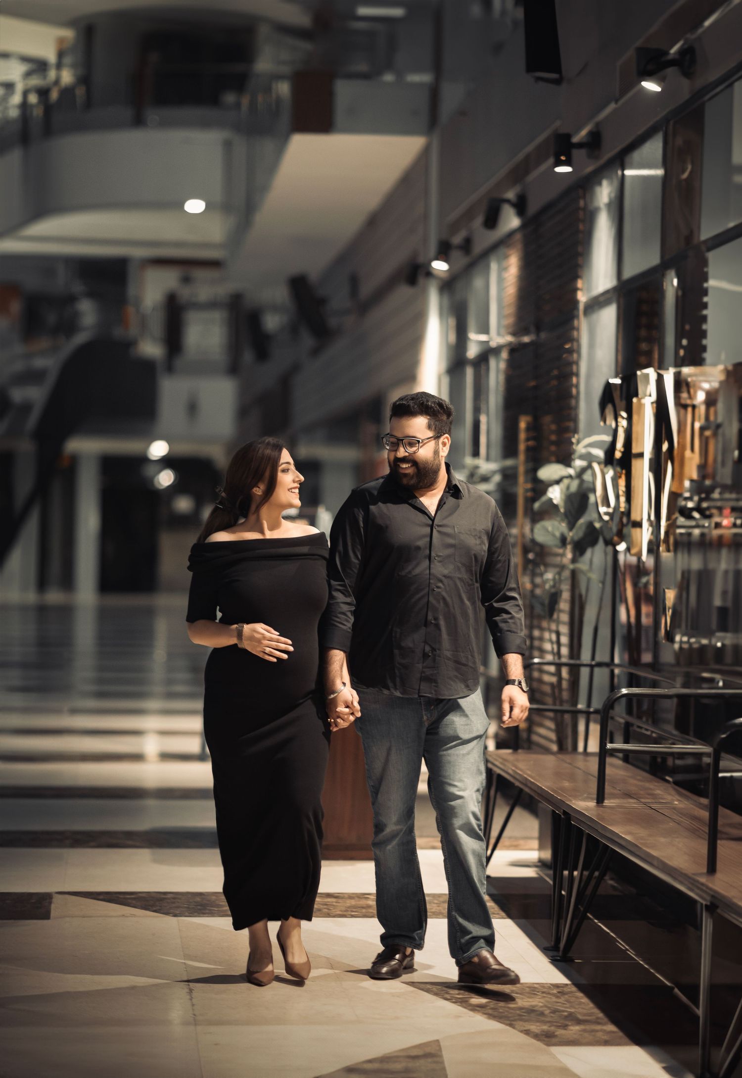 Couple walking together through a dimly lit gallery or shopping mall hallway.