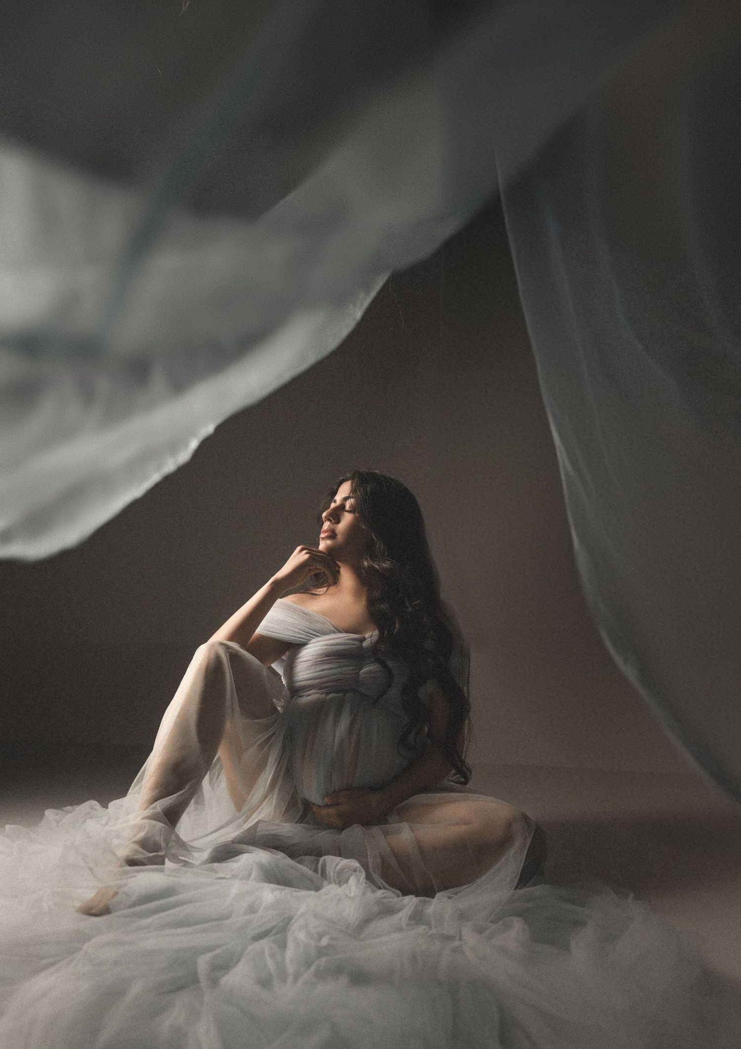 Dramatic maternity photos with flowing white fabric in dark moody setting.