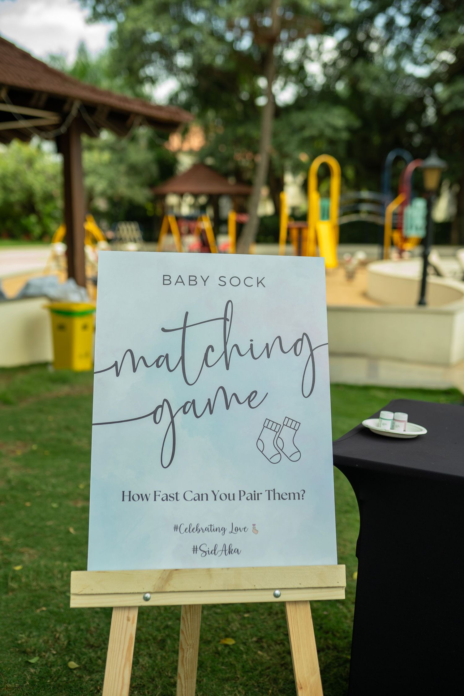Baby sock matching game sign on easel at outdoor baby shower, asking How Fast Can You Pair Them?.