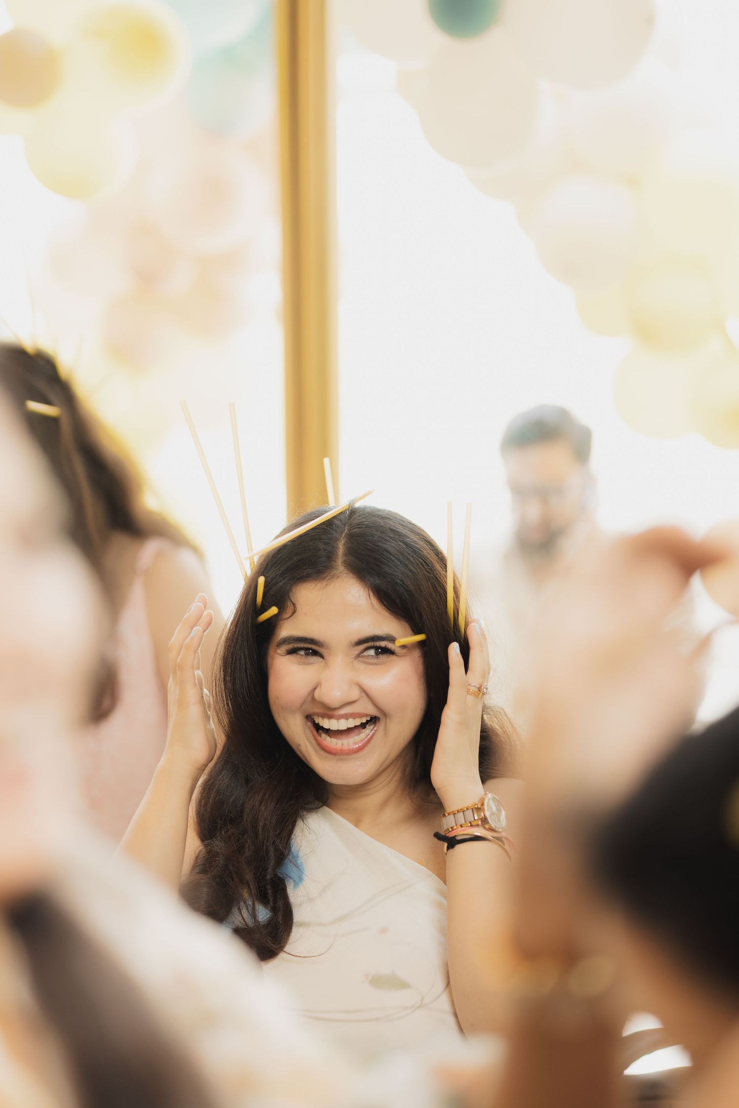 Joyful young woman laughing at a festive party with pastel balloons, confetti in her hair.
