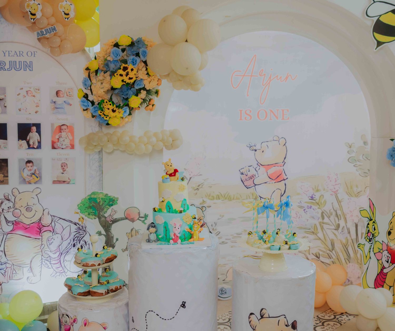 Winnie the Pooh themed first birthday party decoration with cakes and balloon arch.