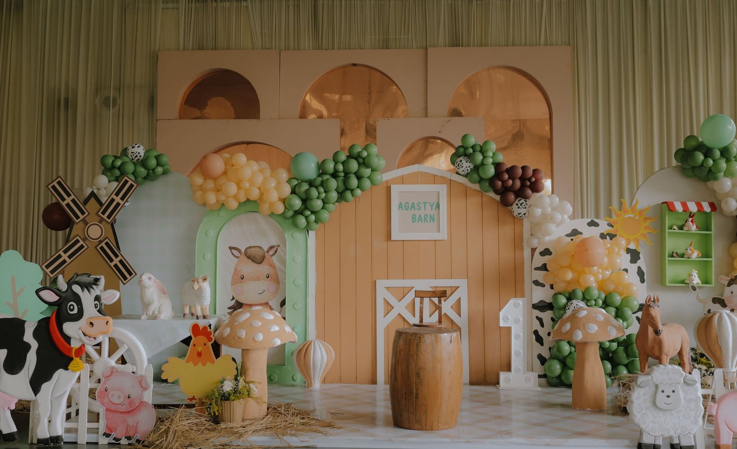 Farm-themed birthday party backdrop with balloon arch, wooden barn, windmill, cow cutouts, and colorful decorations.