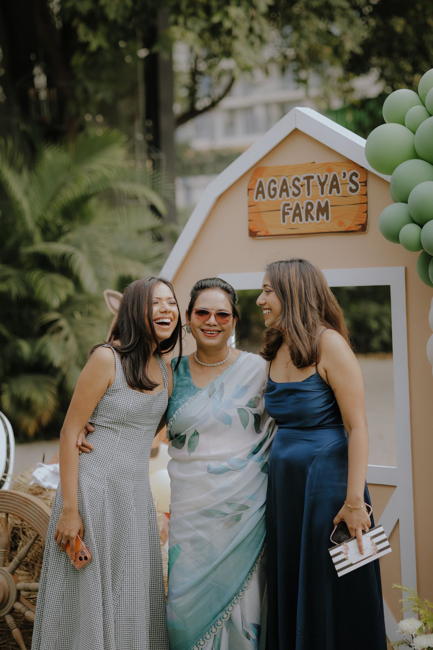 Three women smiling and posing together at Agastya's Farm themed party with green balloon decorations.