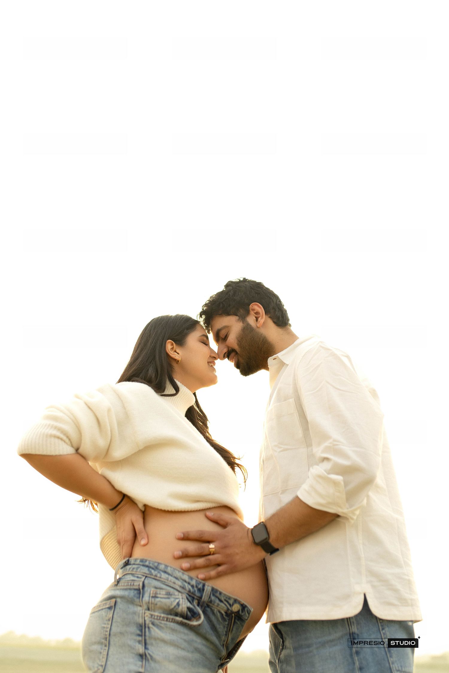Couple sharing intimate moment outdoors, man tenderly holding pregnant woman's baby bump in soft natural light.