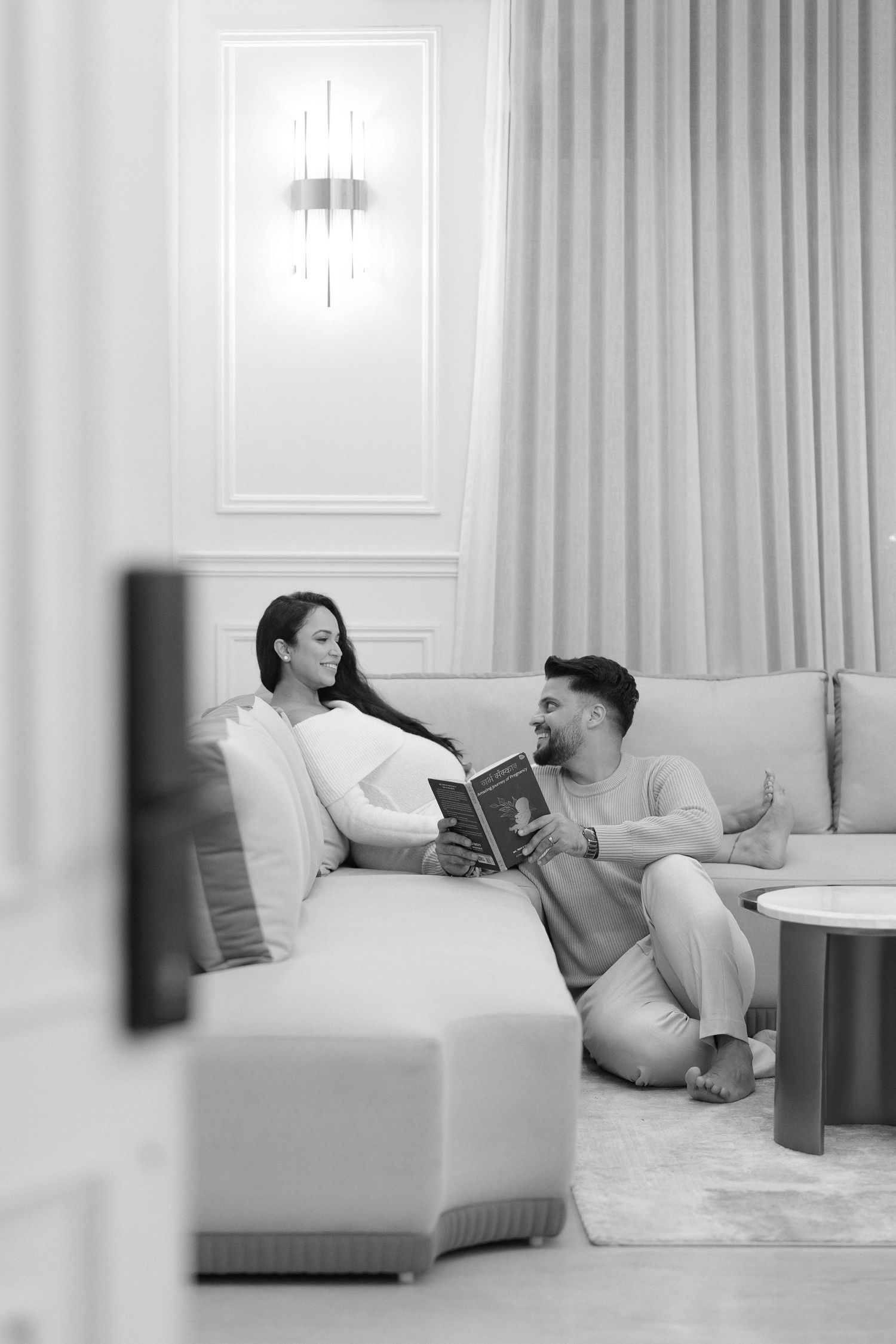 A couple relaxes on a modern sofa, sharing a book in an elegant, softly lit living room.