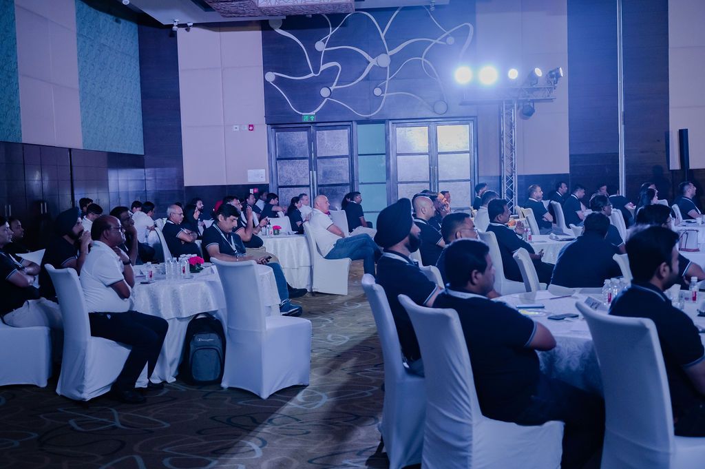 Guests seated at round tables in an elegant banquet hall with white chair covers during a formal corporate dinner event.