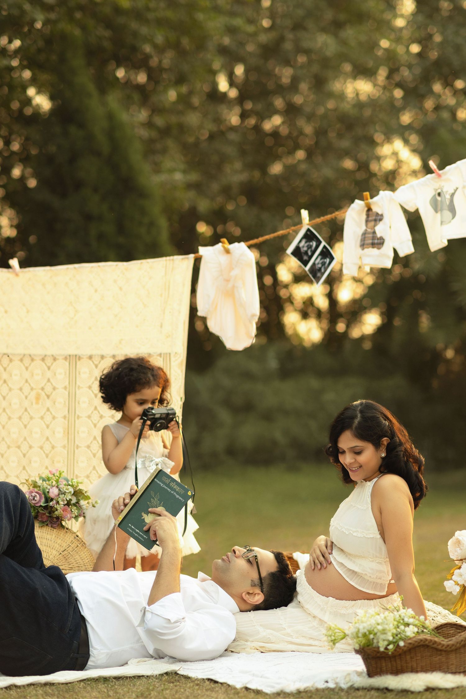 A photographer captures a couple relaxing on a blanket outdoors with laundry hanging on a clothesline in soft sunlight.