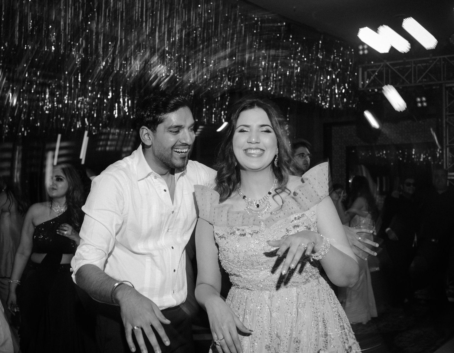 A couple dances and laughs together under sparkling decorative lights at a celebration event.