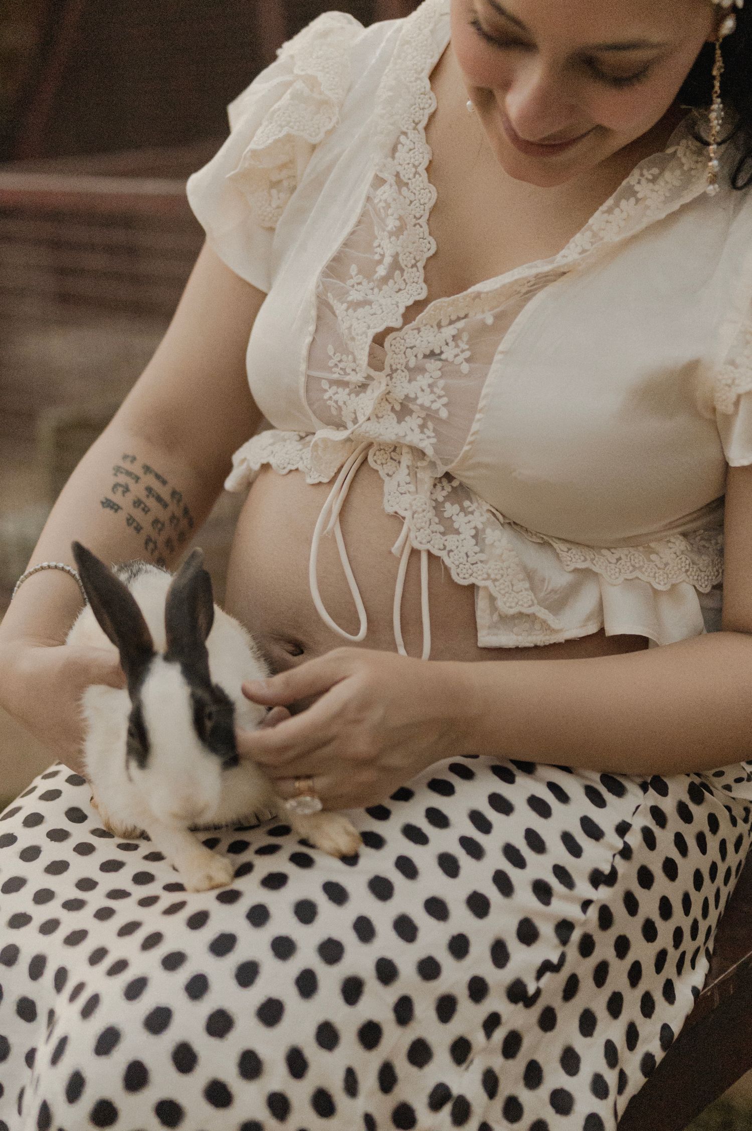 Pregnant woman in lace crop top holding a black and white bunny on her polka dot skirt.