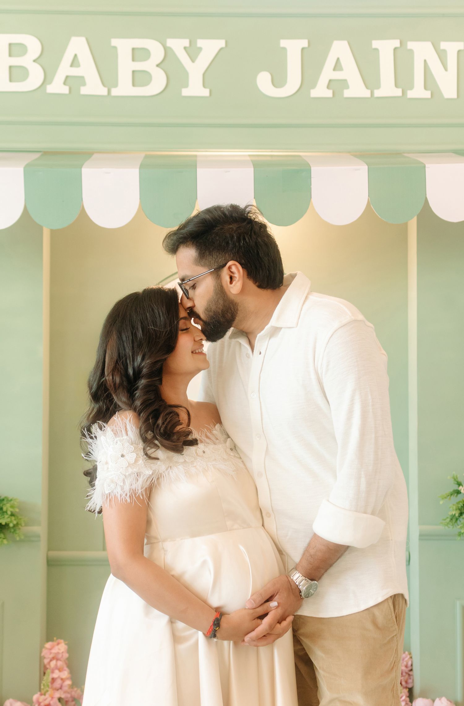 Expecting couple shares a tender moment in front of a mint green Baby Jain sign at a maternity photo shoot.