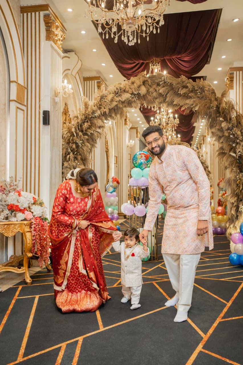 Indian family in traditional attire celebrating a baby's first birthday at an elegant decorated venue with balloons.