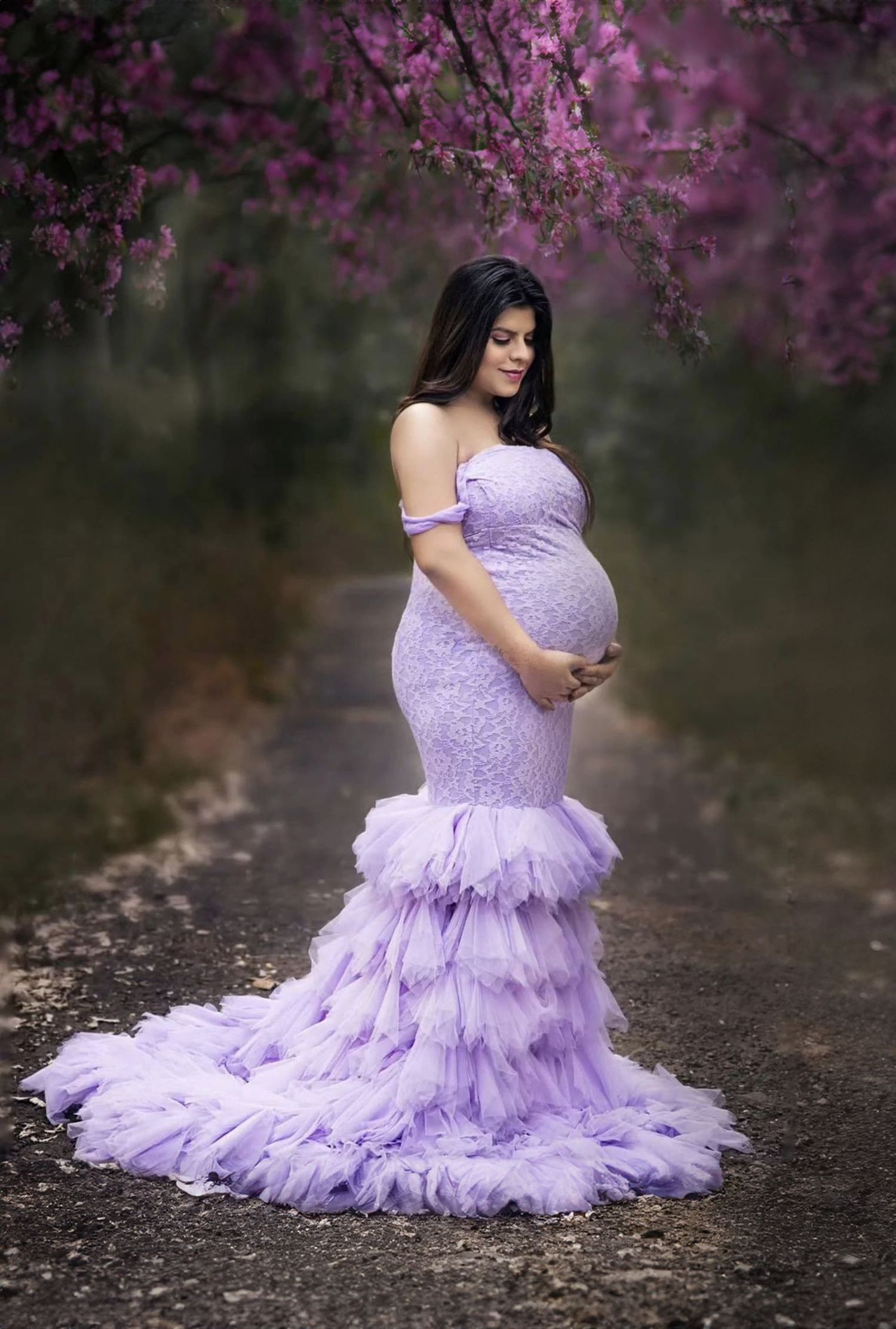 Ethereal maternity photography against purple blossoms featuring a flowing lilac gown with ruffled details.