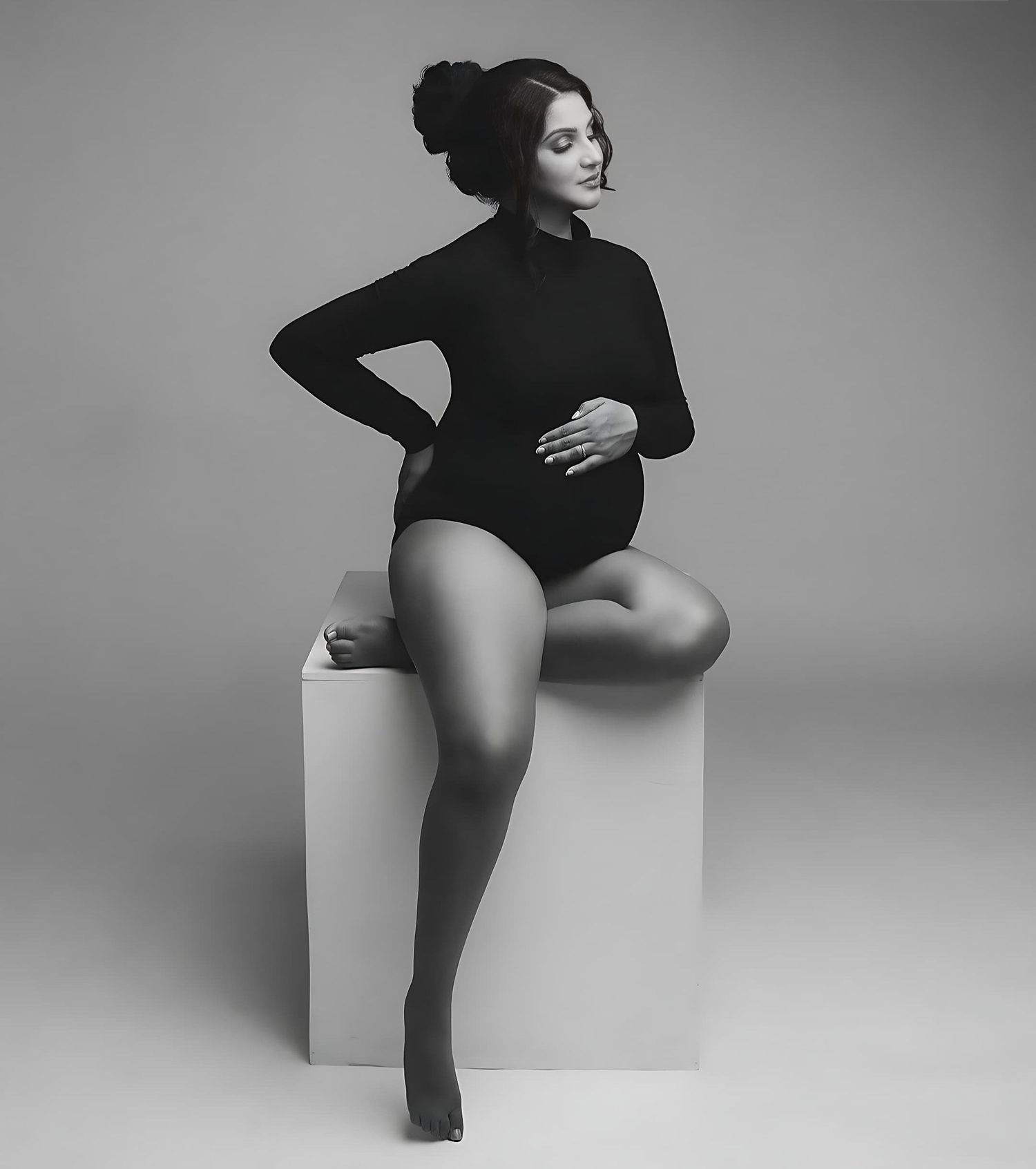Black and white maternity portrait on white cube with minimalist styling.