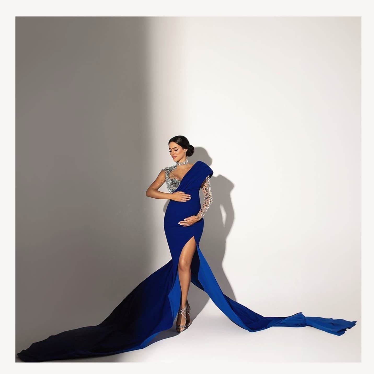 Elegant royal blue maternity gown with dramatic flowing train and thigh-high slit photographed against white backdrop.