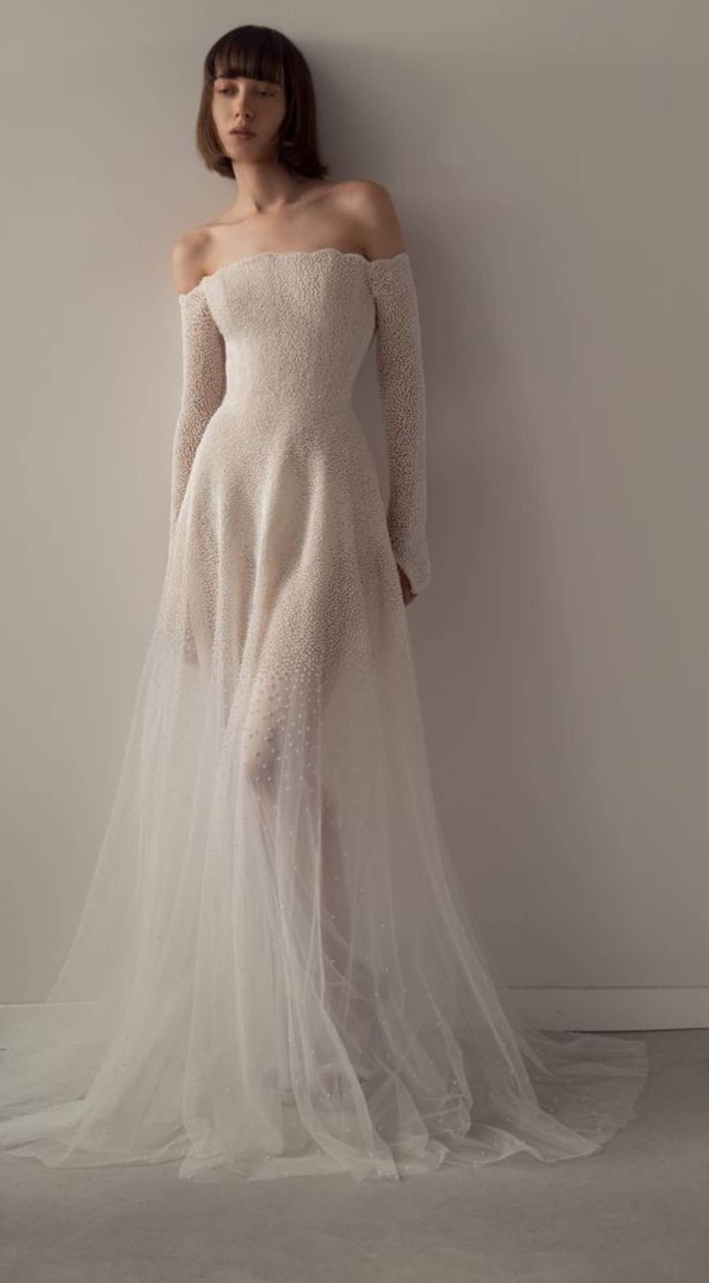 Elegant off-shoulder wedding dress with fitted bodice and flowing tulle skirt in a minimalist setting.