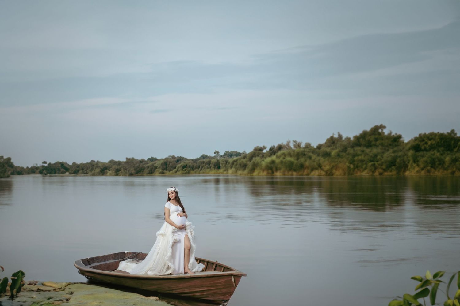 Dreamy maternity photo on wooden boat in serene lake setting.