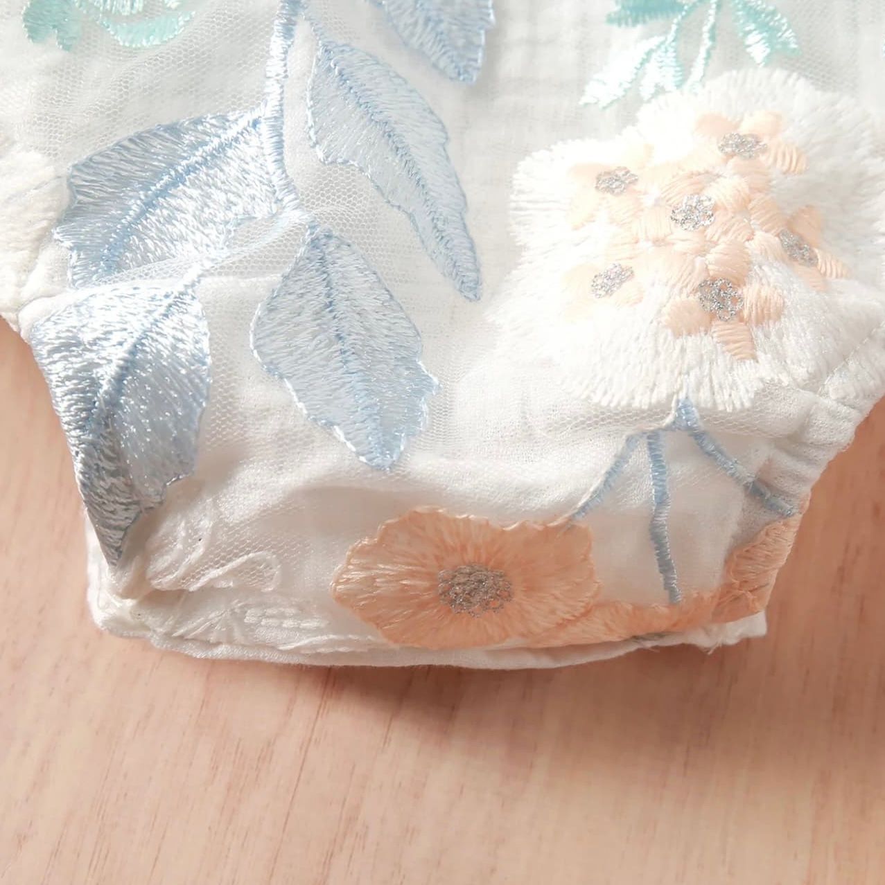 Close-up view of silver and peach floral pattern on white fabric showing delicate metallic leaf designs.