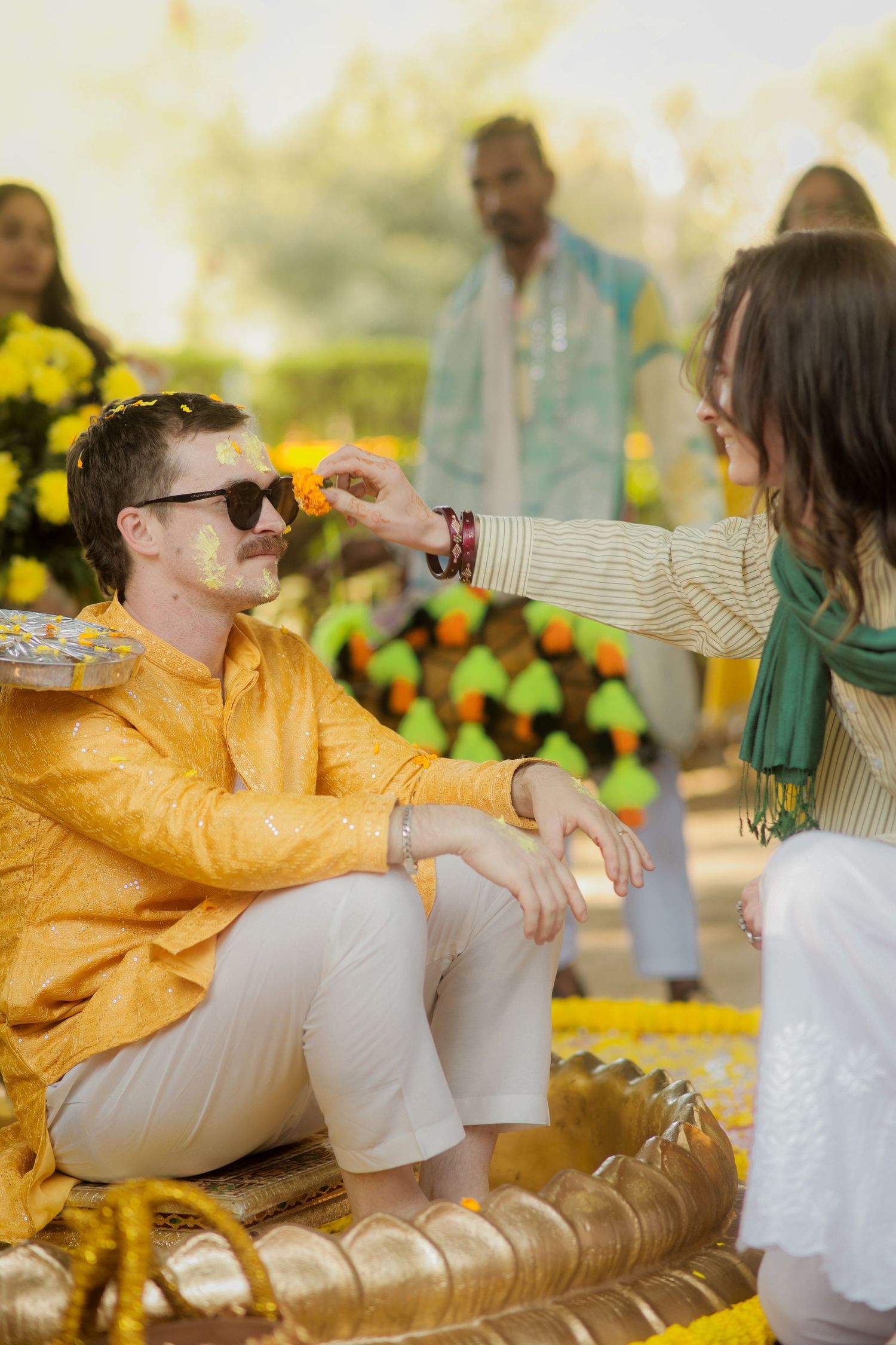 A person in a yellow jacket lounges casually on a bench during a sunny outdoor gathering.