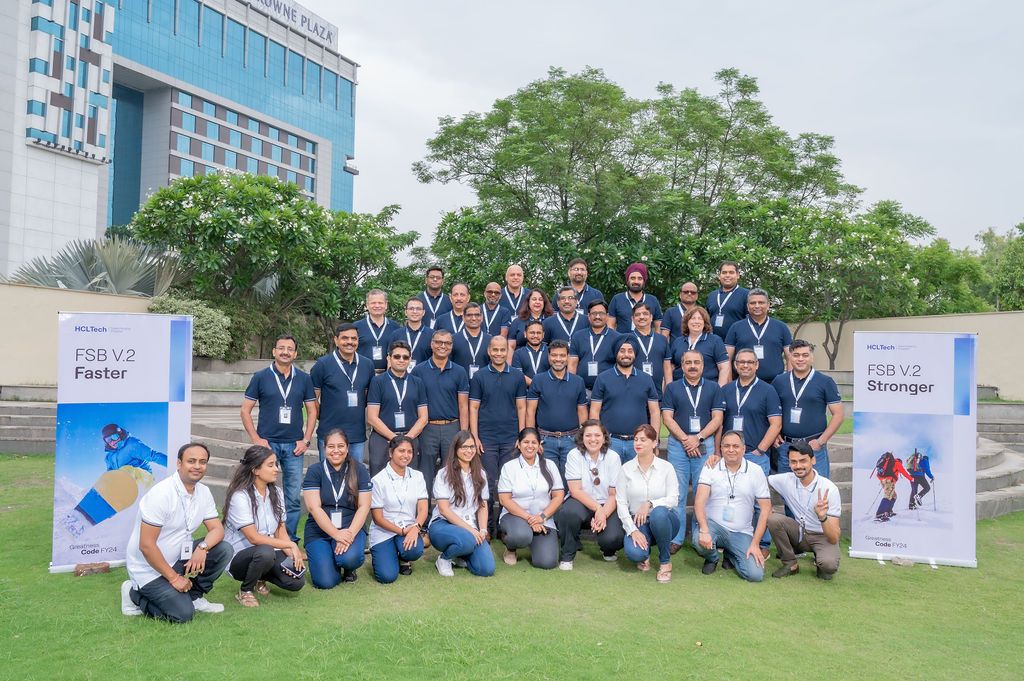 Large group of professionals pose outdoors at FSB V2 corporate event with banners reading Faster and Stronger.